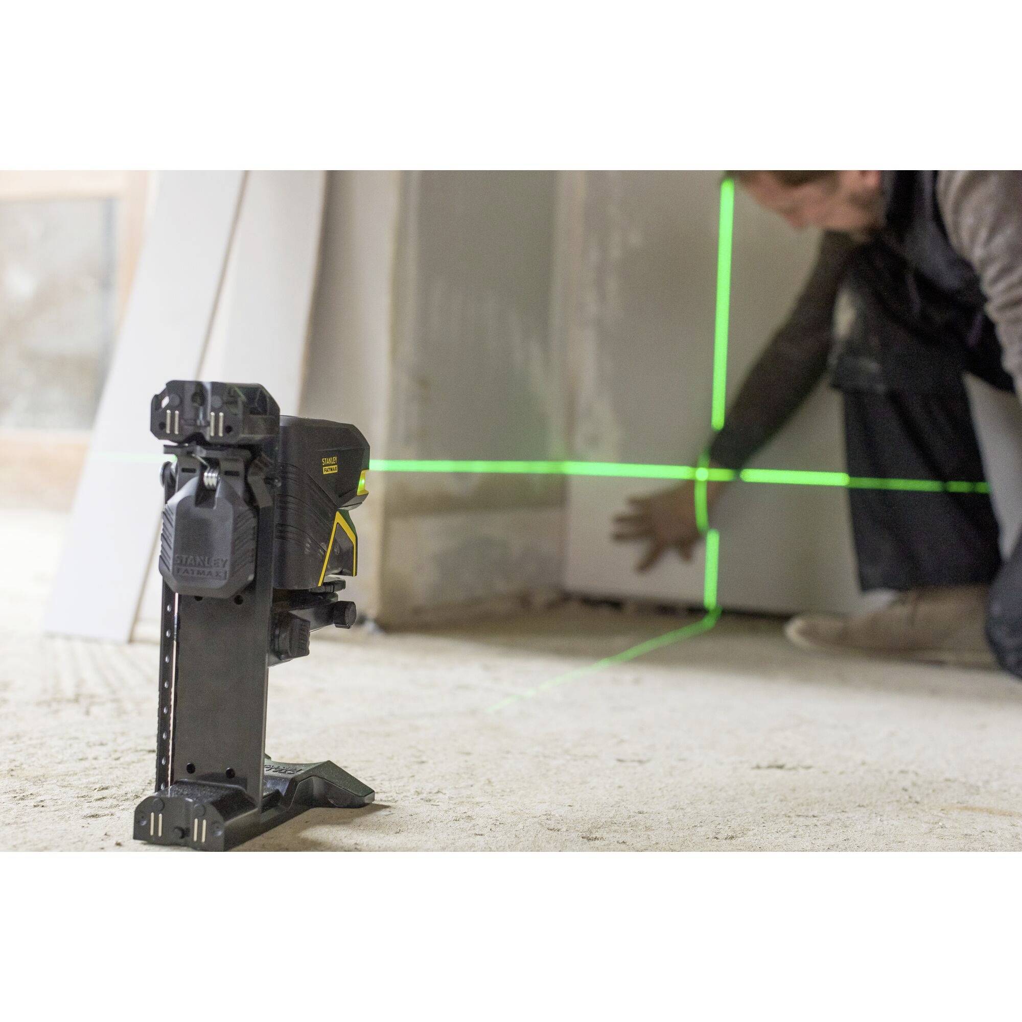 A tradesman is checking the wall surface in an interior space using a green cross-line laser. The laser projects lines for alignment purposes.