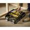 An open toolbox on the floor with yellow hand tools and accessories. A person in workwear is reaching for tools.
