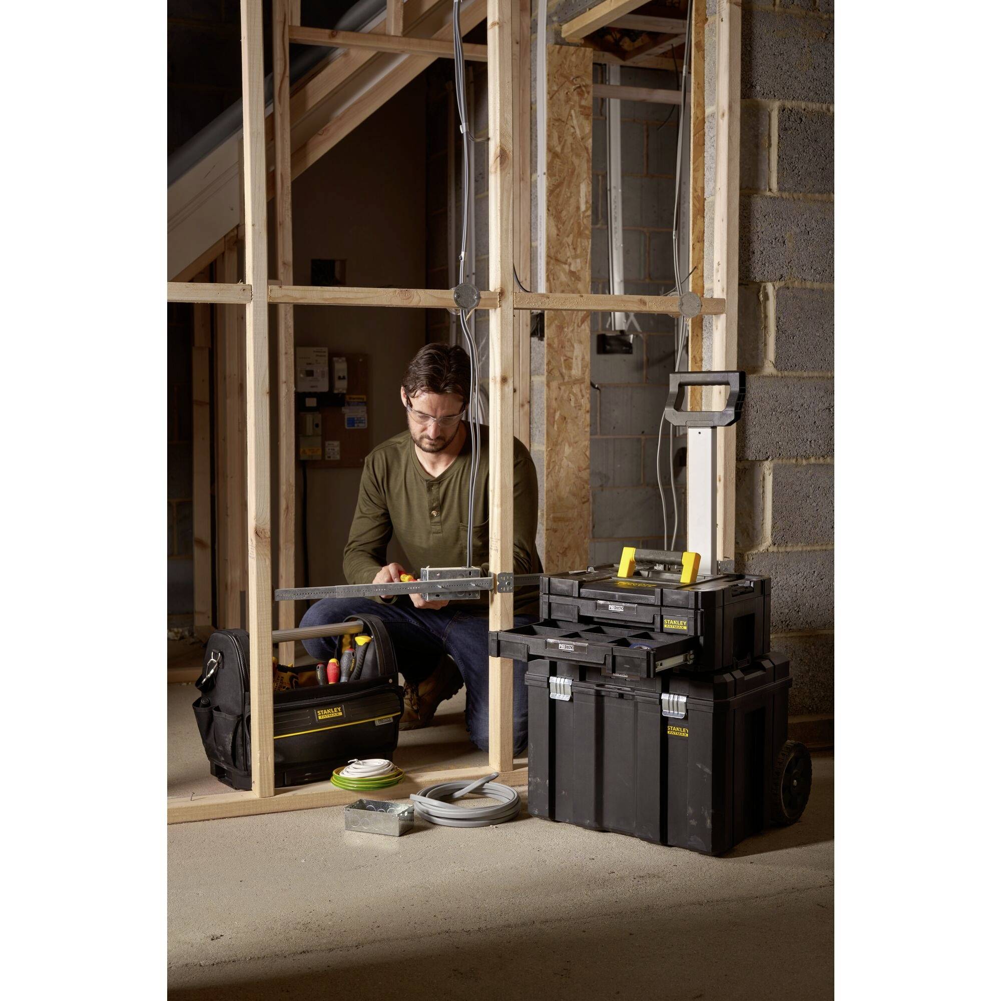 A man is working in an unfinished building, surrounded by tool cases and construction materials. He is focused on a project.