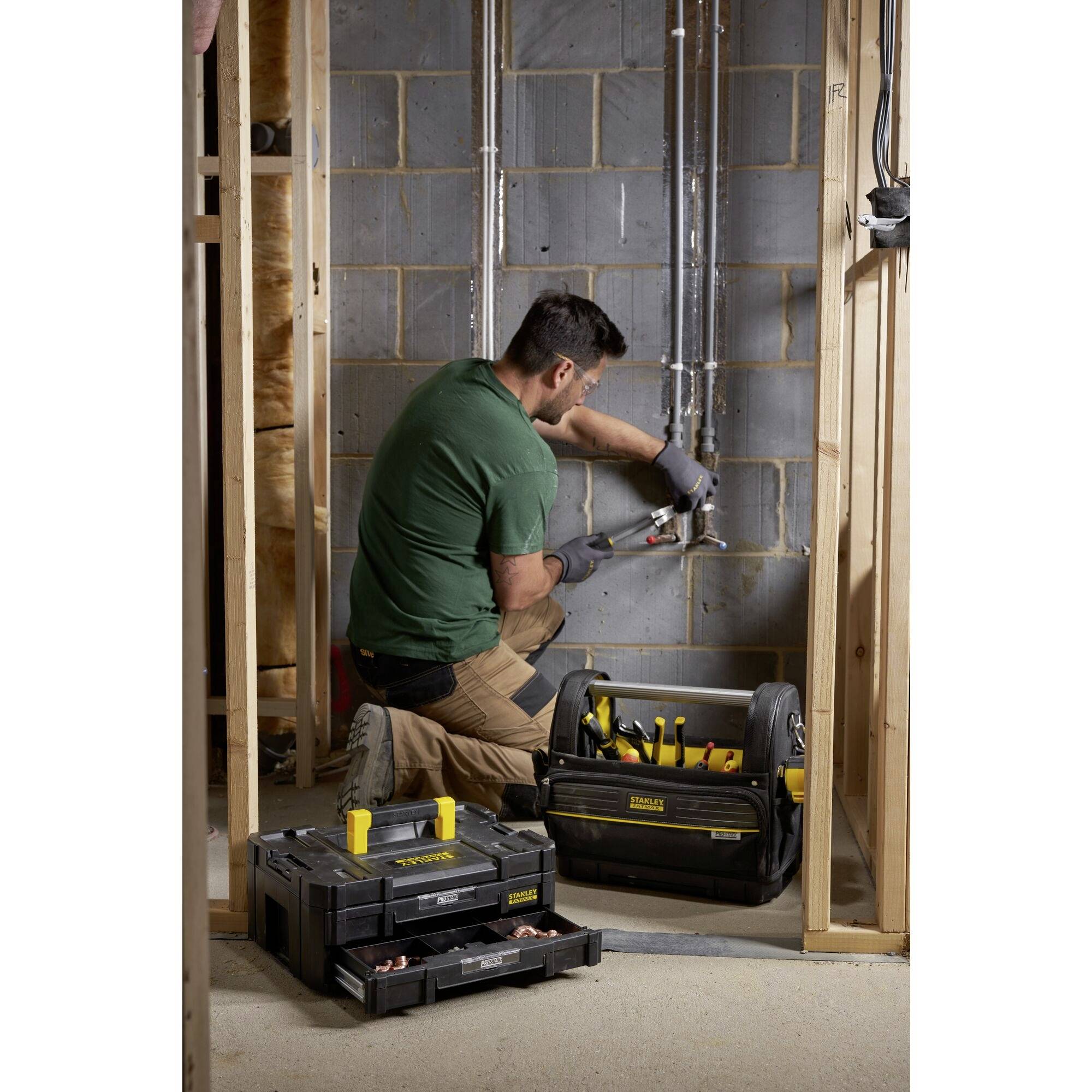 A tradesman in green clothing is installing a cable in an unfinished room. Tools and boxes are present on the floor.