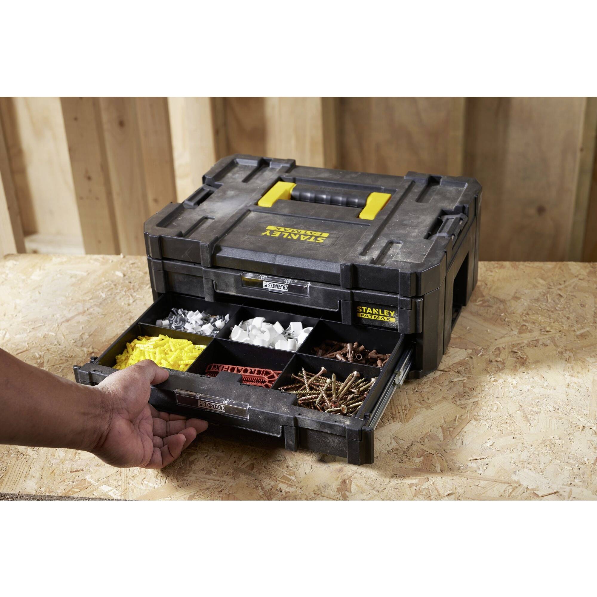 'Open toolbox with a yellow handle and drawers displaying sorted screws, wall plugs, and nuts. A hand pulls out a drawer.'