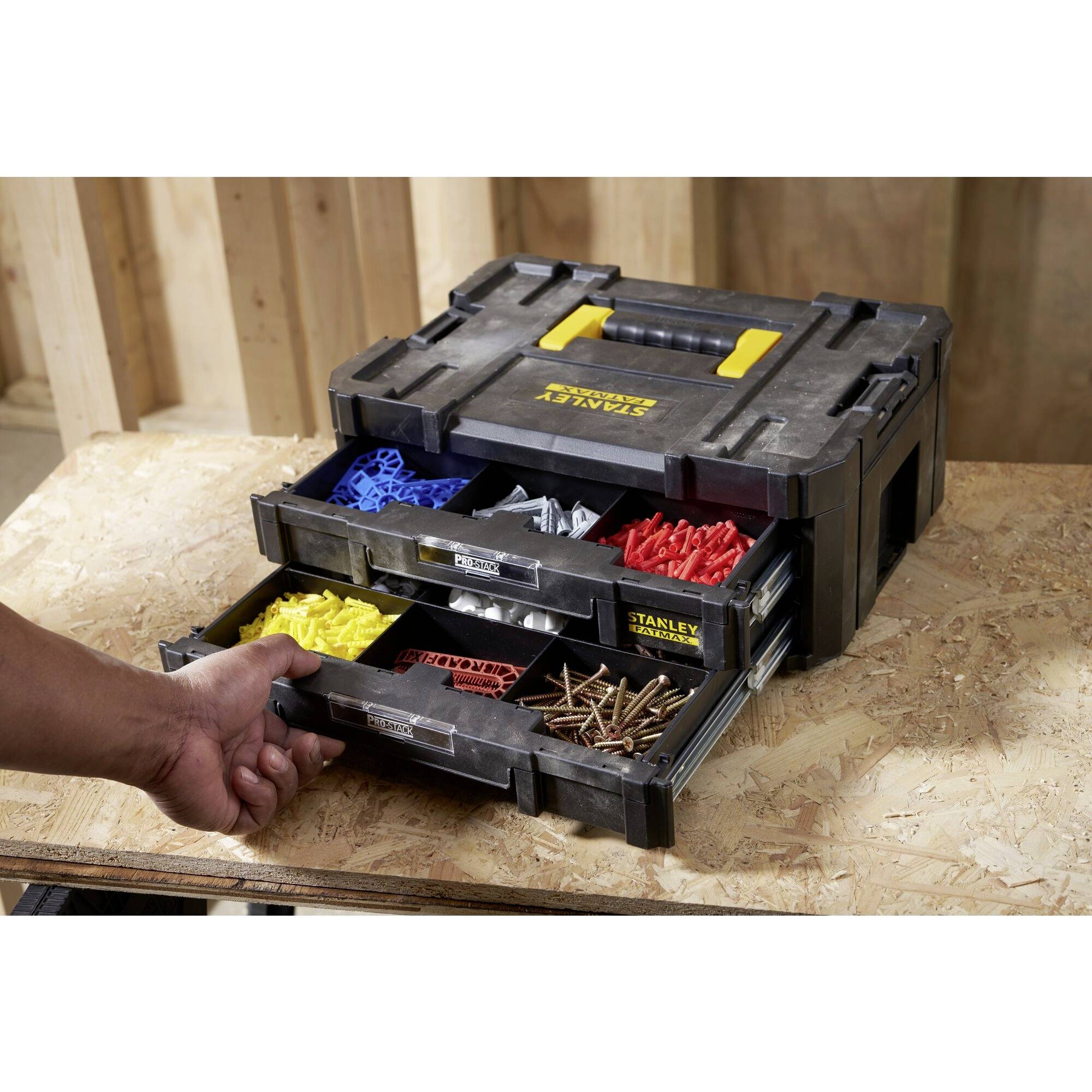 A black toolbox with multiple drawers, filled with sorted plastic wall plugs and screws in various colours. A hand pulls out one of the drawers.