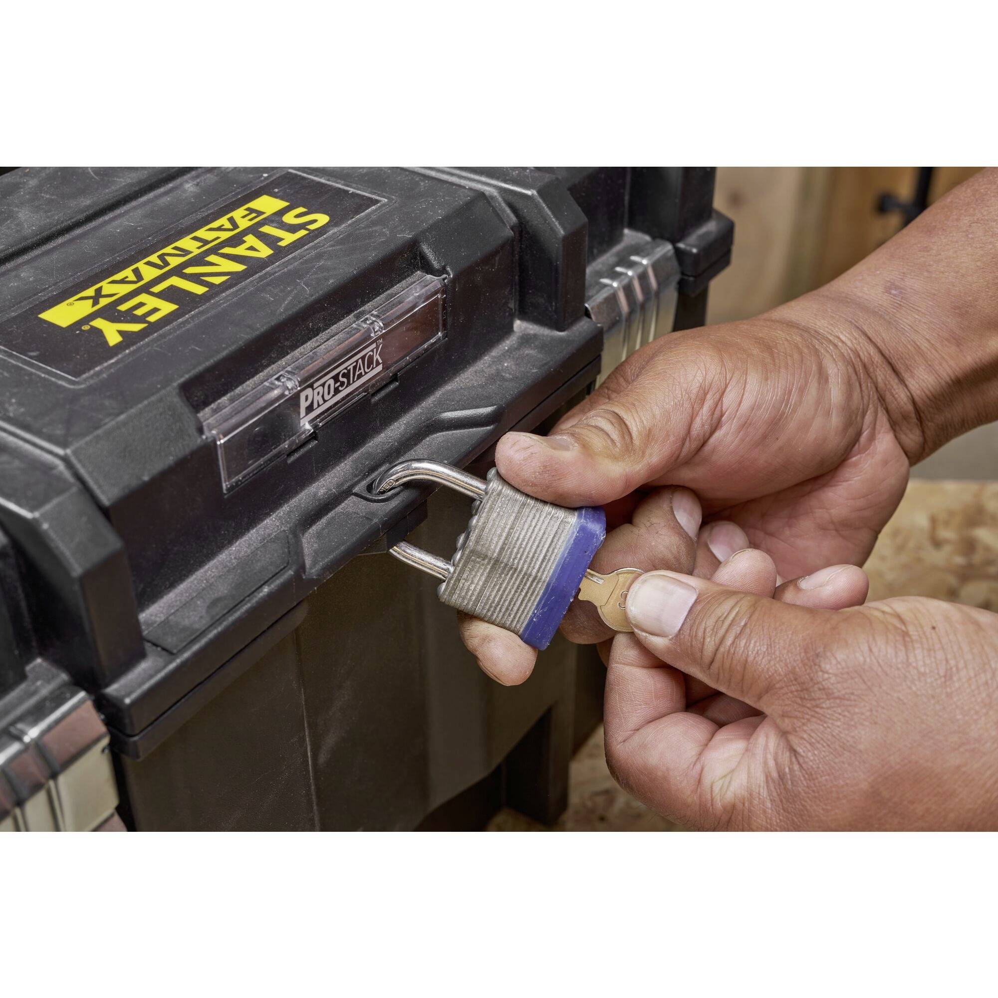 A person unlocks a padlock on a black toolbox with a key.