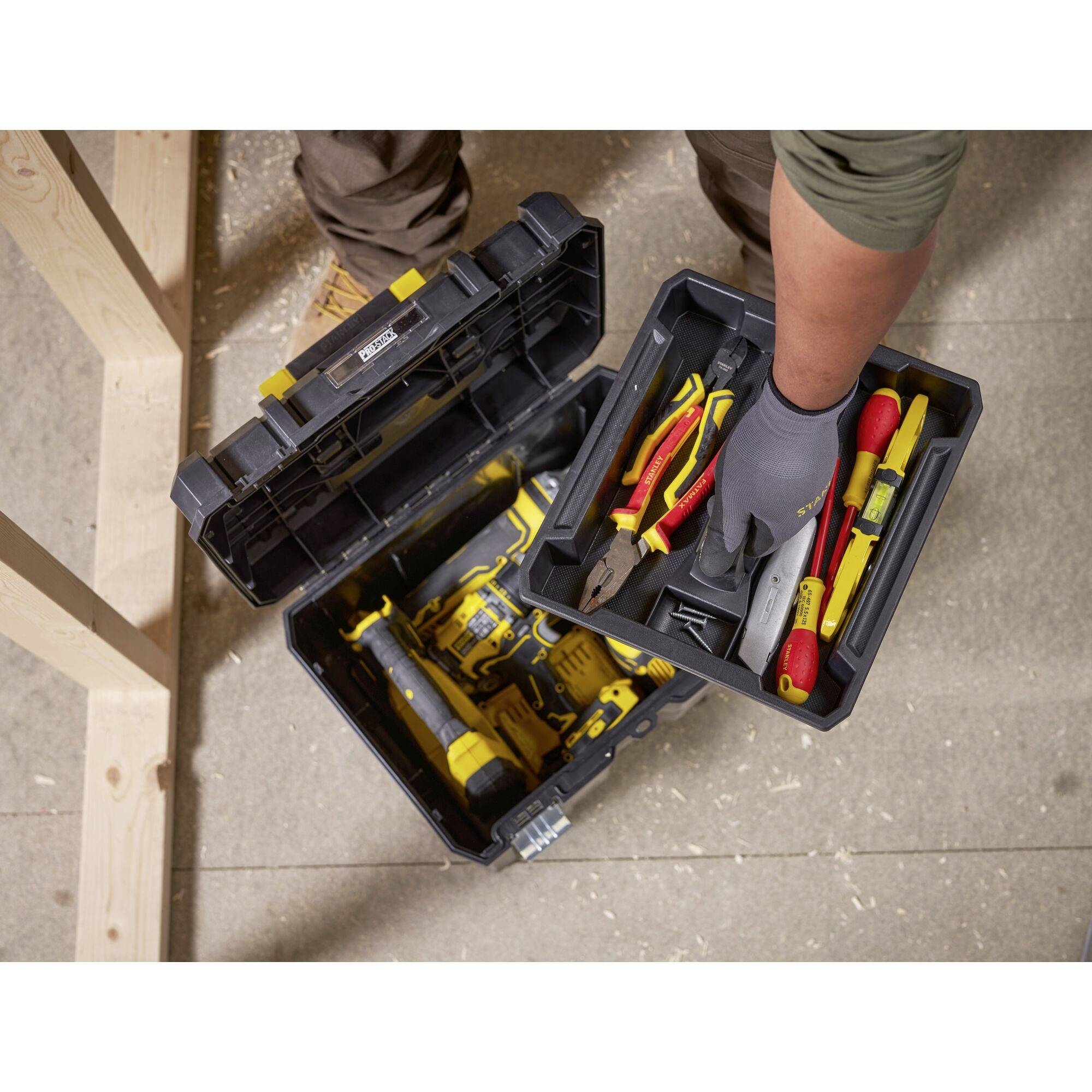 A person is removing tools from an open toolbox. Included are pliers, screwdrivers and a cordless drill.