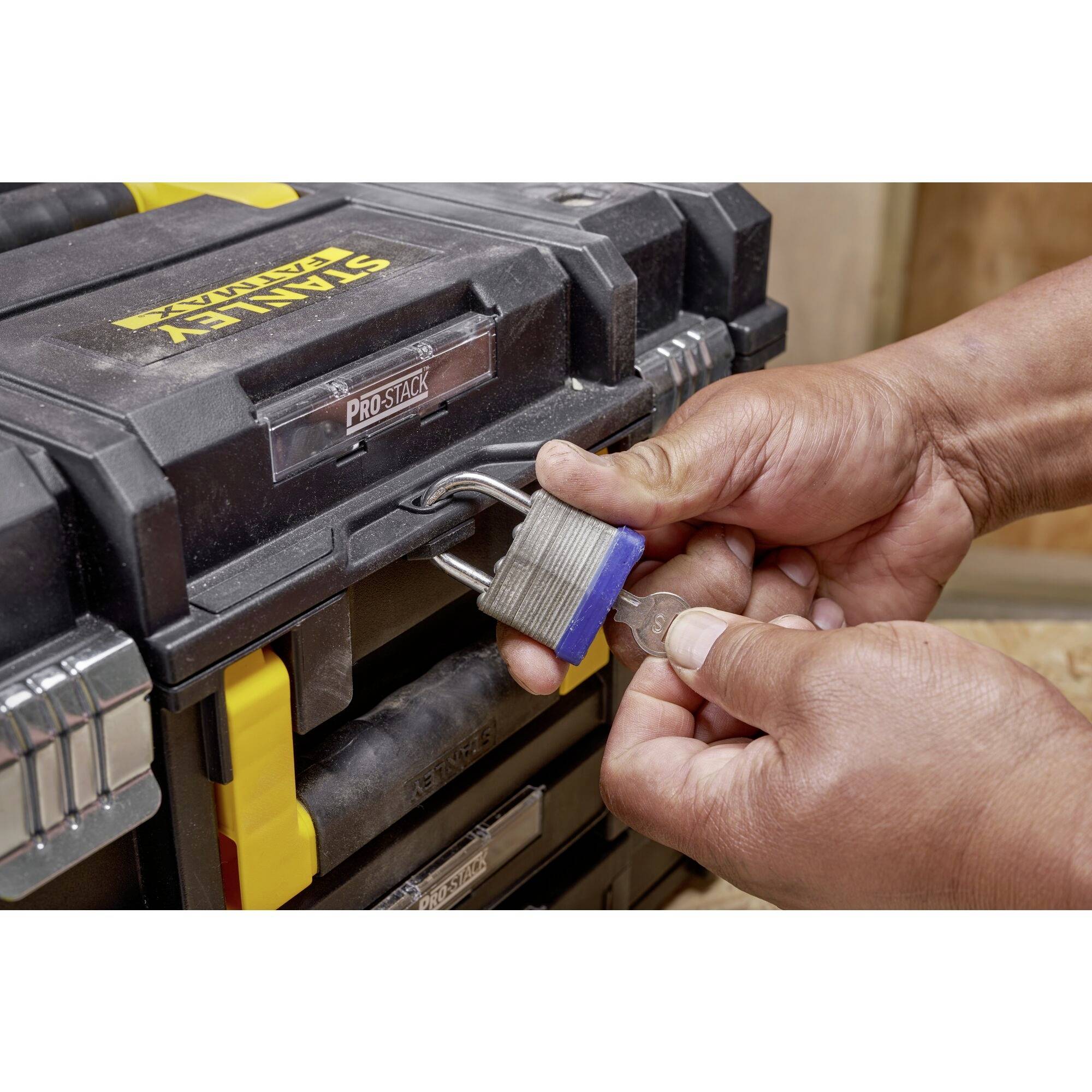 A person is unlocking a padlock on a black toolbox with yellow handles.