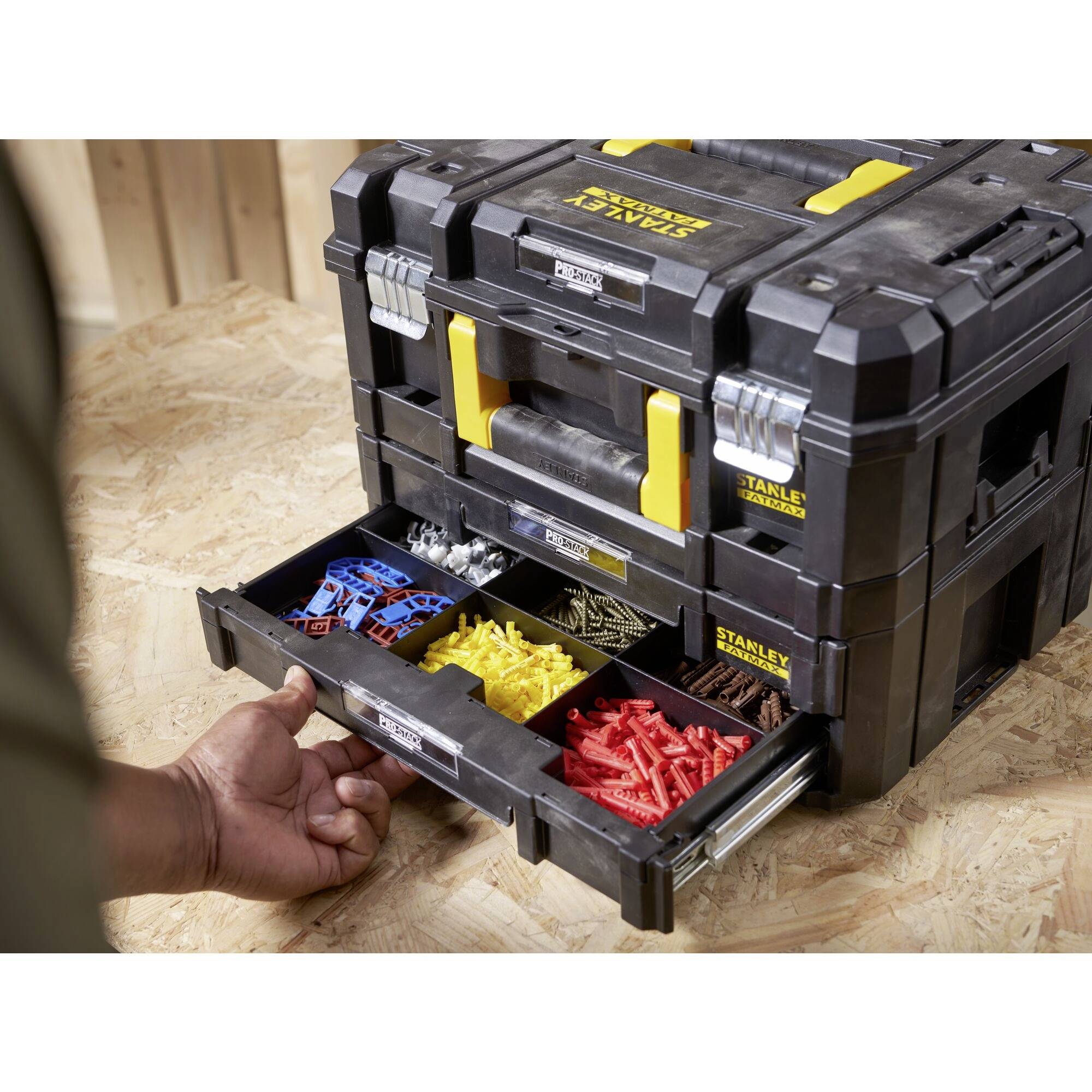 A person opens a drawer of a black toolbox, which is equipped with yellow and red wall plugs and other fastening materials.