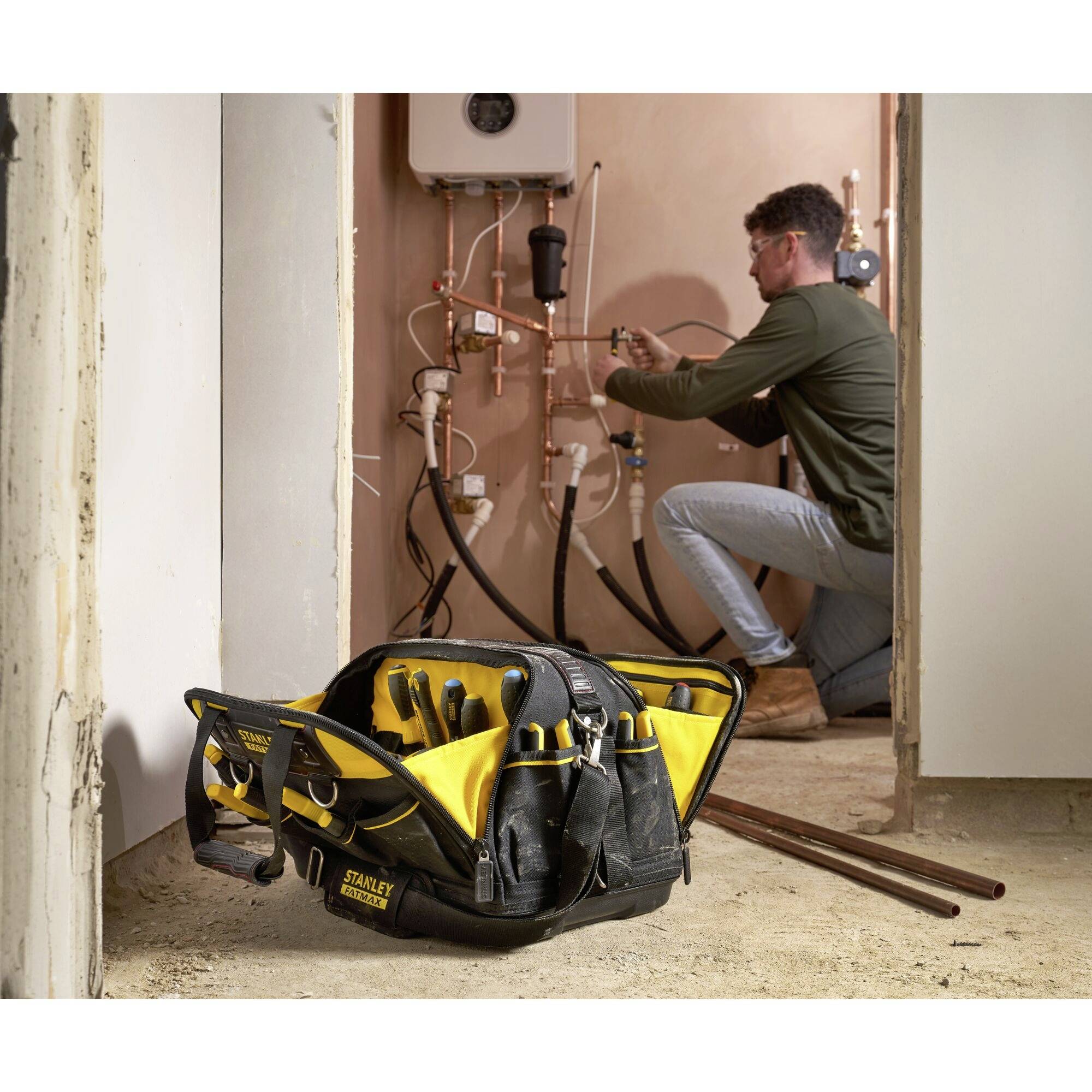 A tradesman is repairing pipes in a boiler room. A toolbox with various tools is in the foreground.