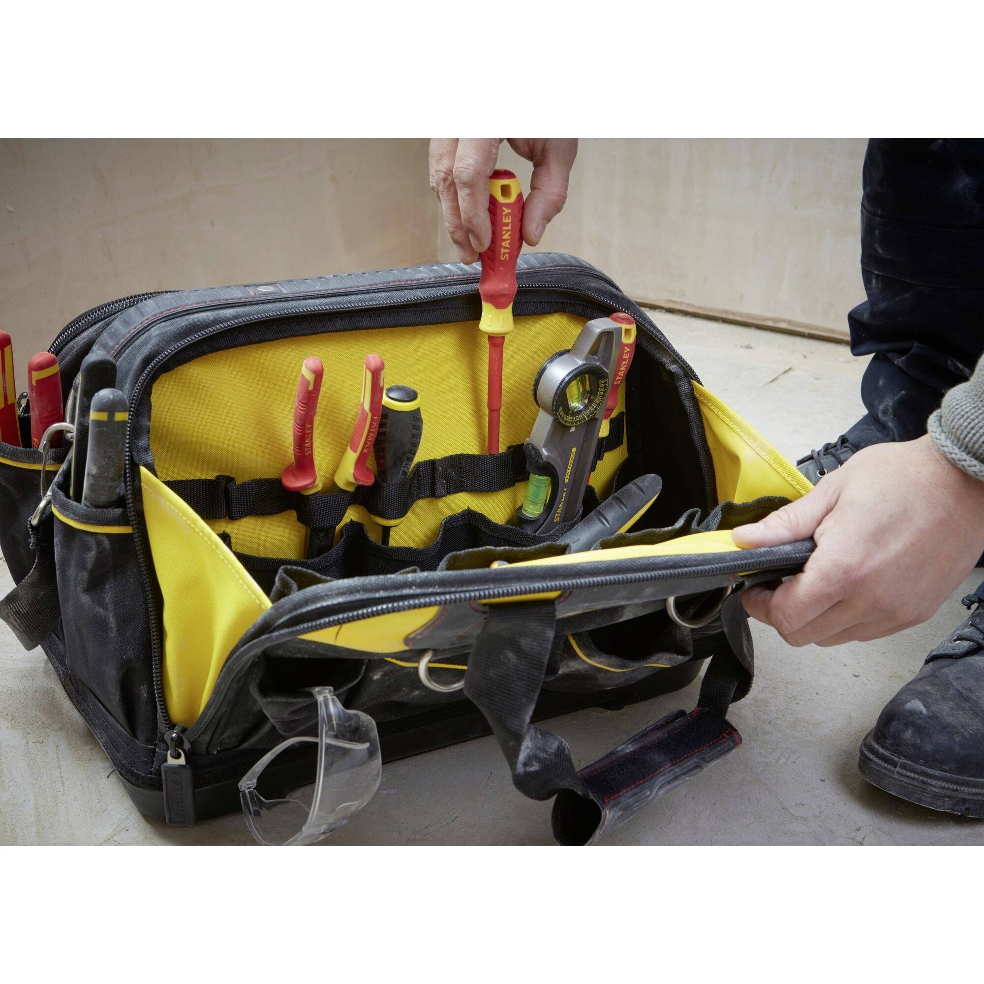An open tool bag with various hand tools such as screwdrivers and pliers. Two hands are organising the tools.