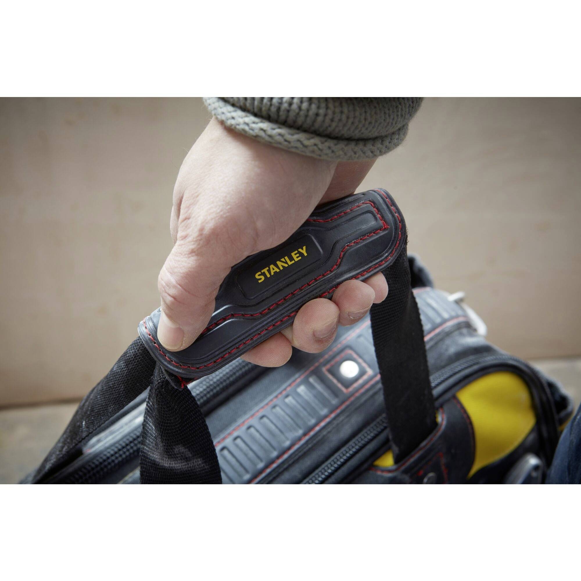 A hand is gripping the handle of a Stanley tool case. The case is partially visible and appears ready for transport.