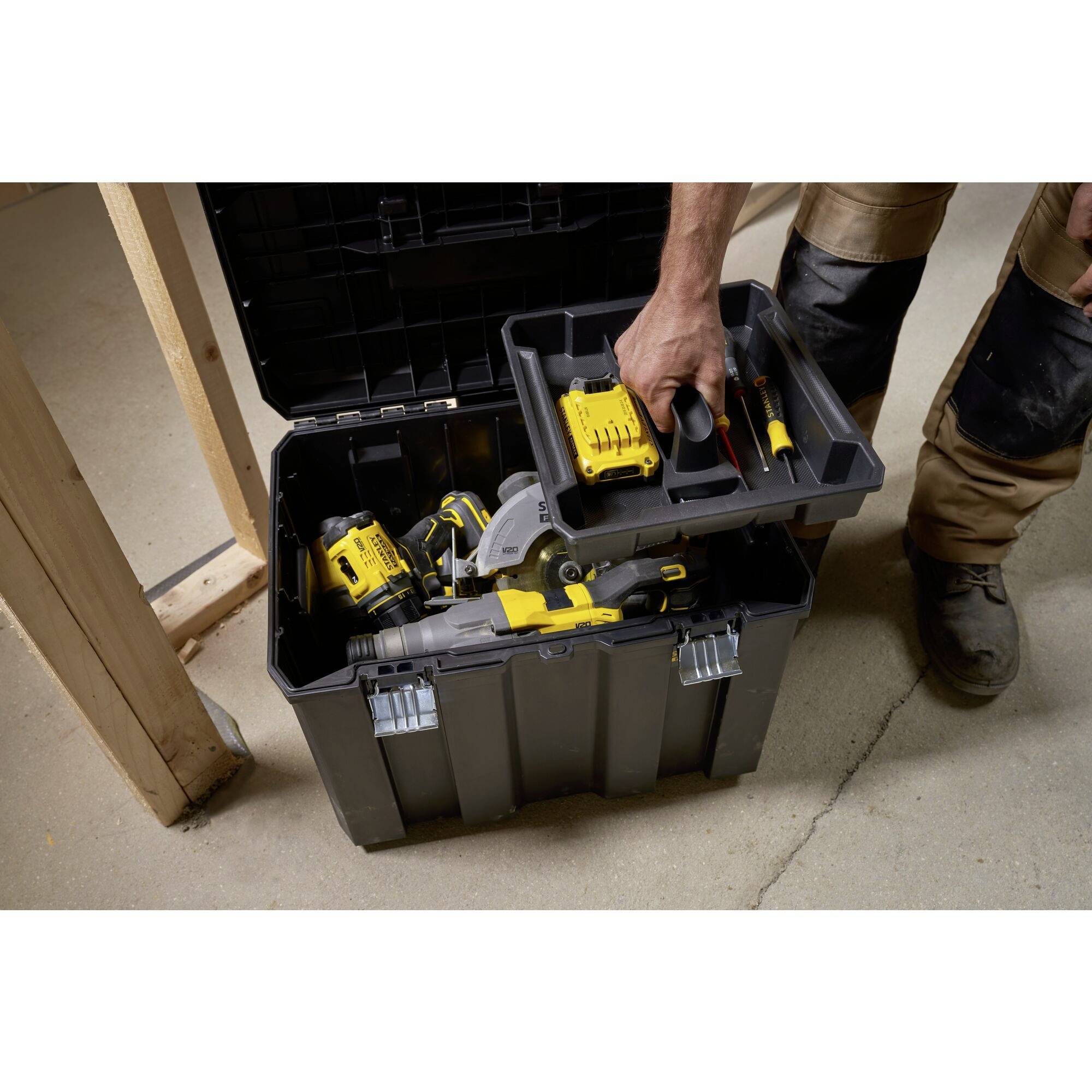 'A man reaches into a toolbox containing a variety of hand tools in a workshop or construction site.'