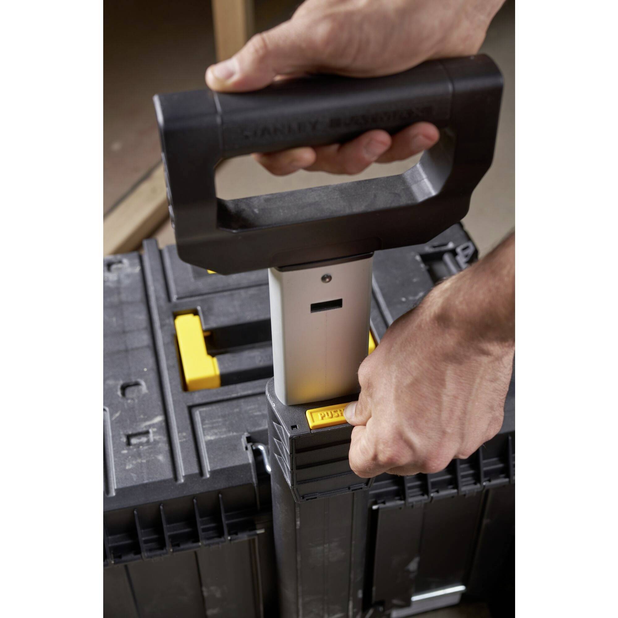 A person pulls up the handle of a tool storage case to open or transport it.