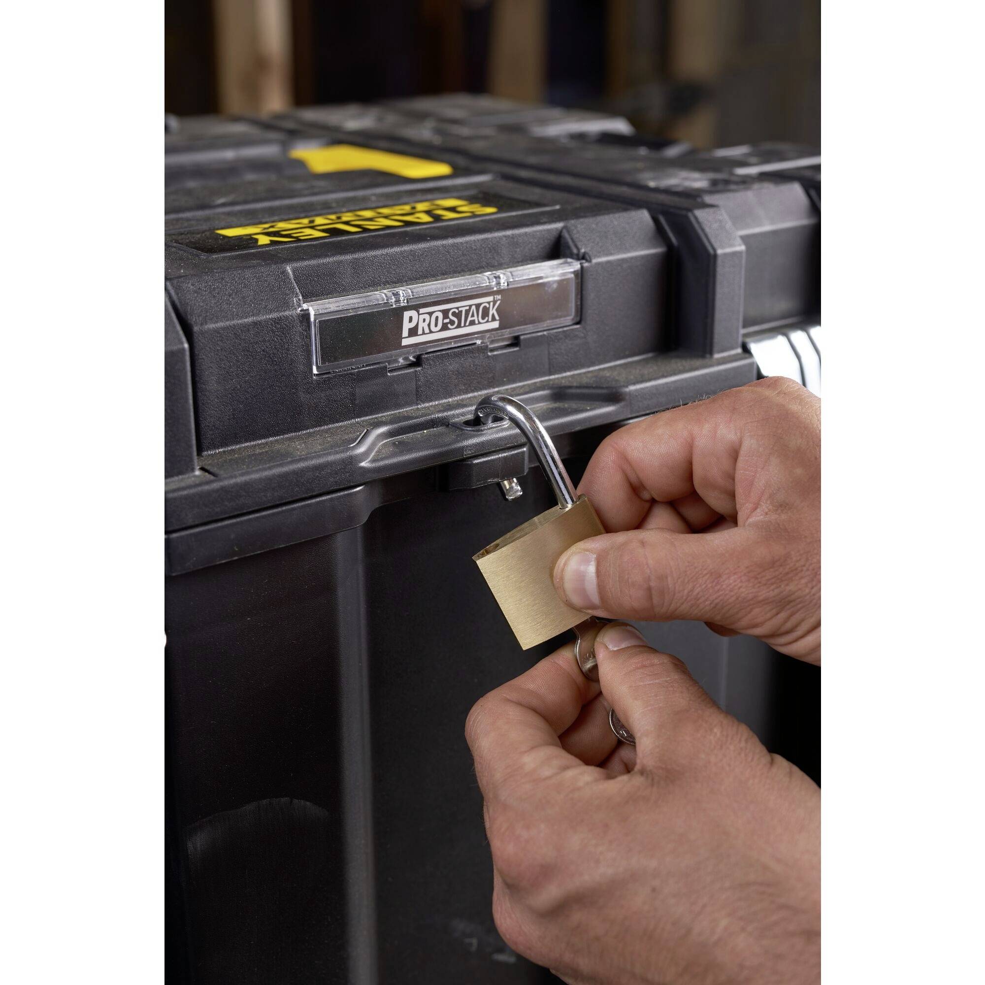 A hand locks a padlock on a robust, secured toolbox. The box bears the 'Pro-Stack' logo.