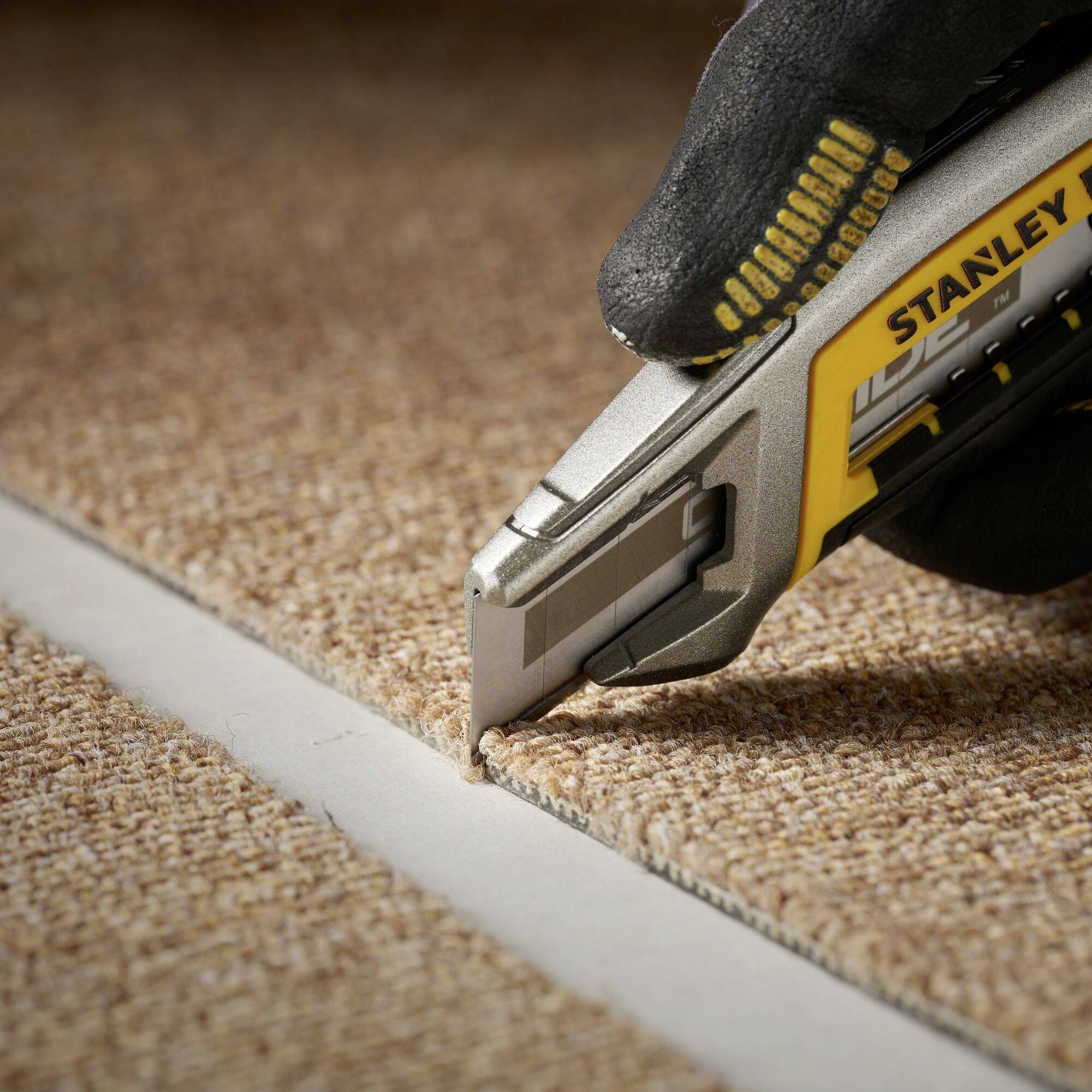 A person is cutting a carpet along an edge with a carpet knife.