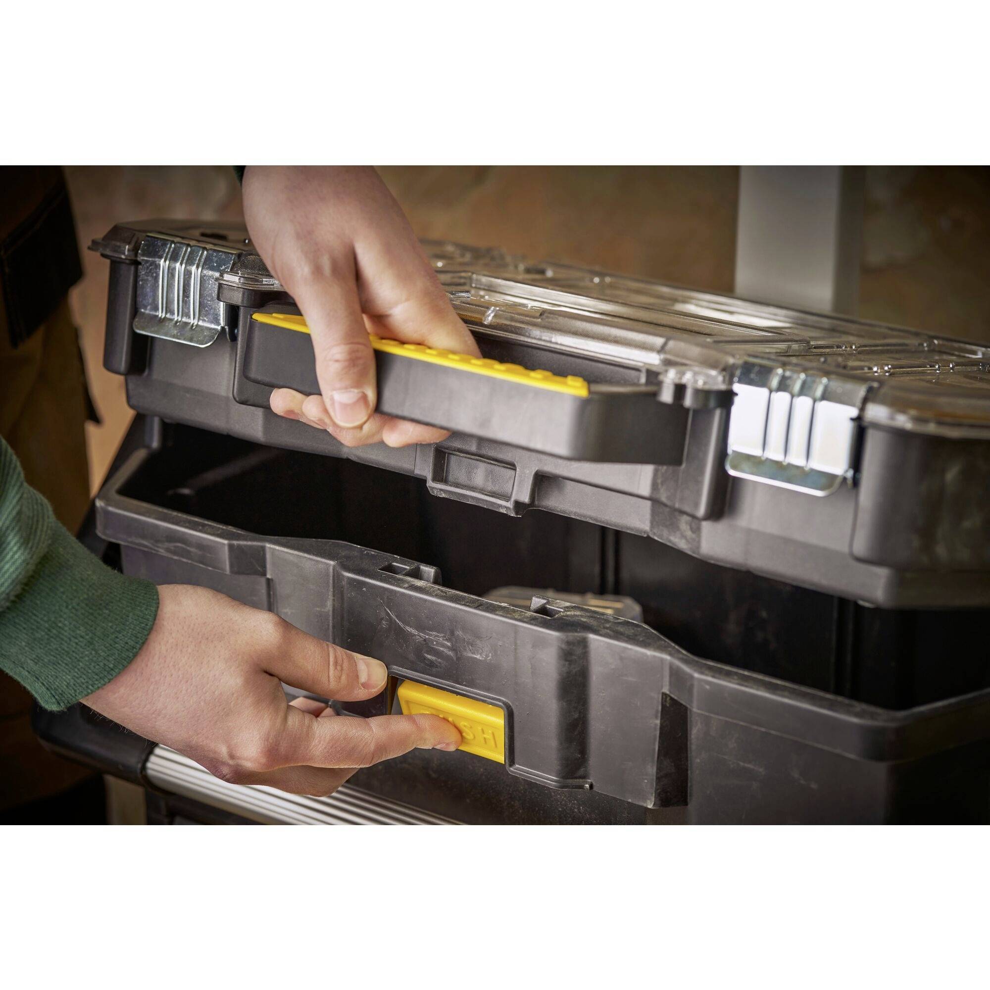 Someone opens a plastic toolbox with metal latches and a yellow handle.