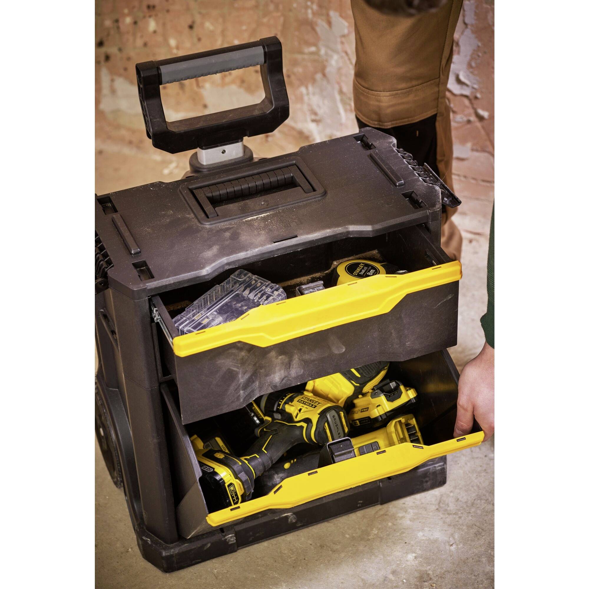 An open toolbox with yellow drawers full of tools, including drills. An unfinished wall can be seen in the background.