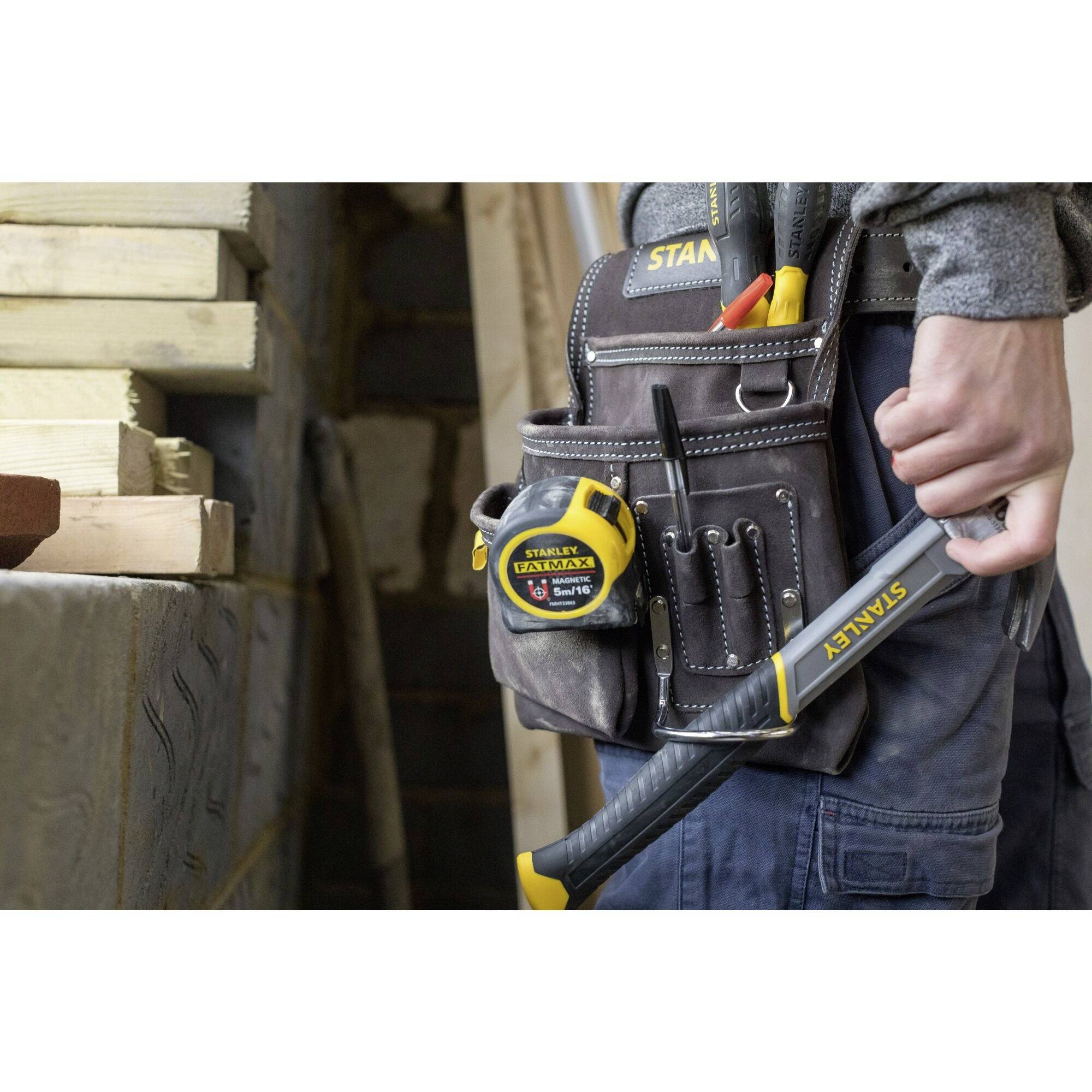 A person is wearing a tool belt with screwdrivers, tape measure and hammer, ready for construction work in a workshop environment.