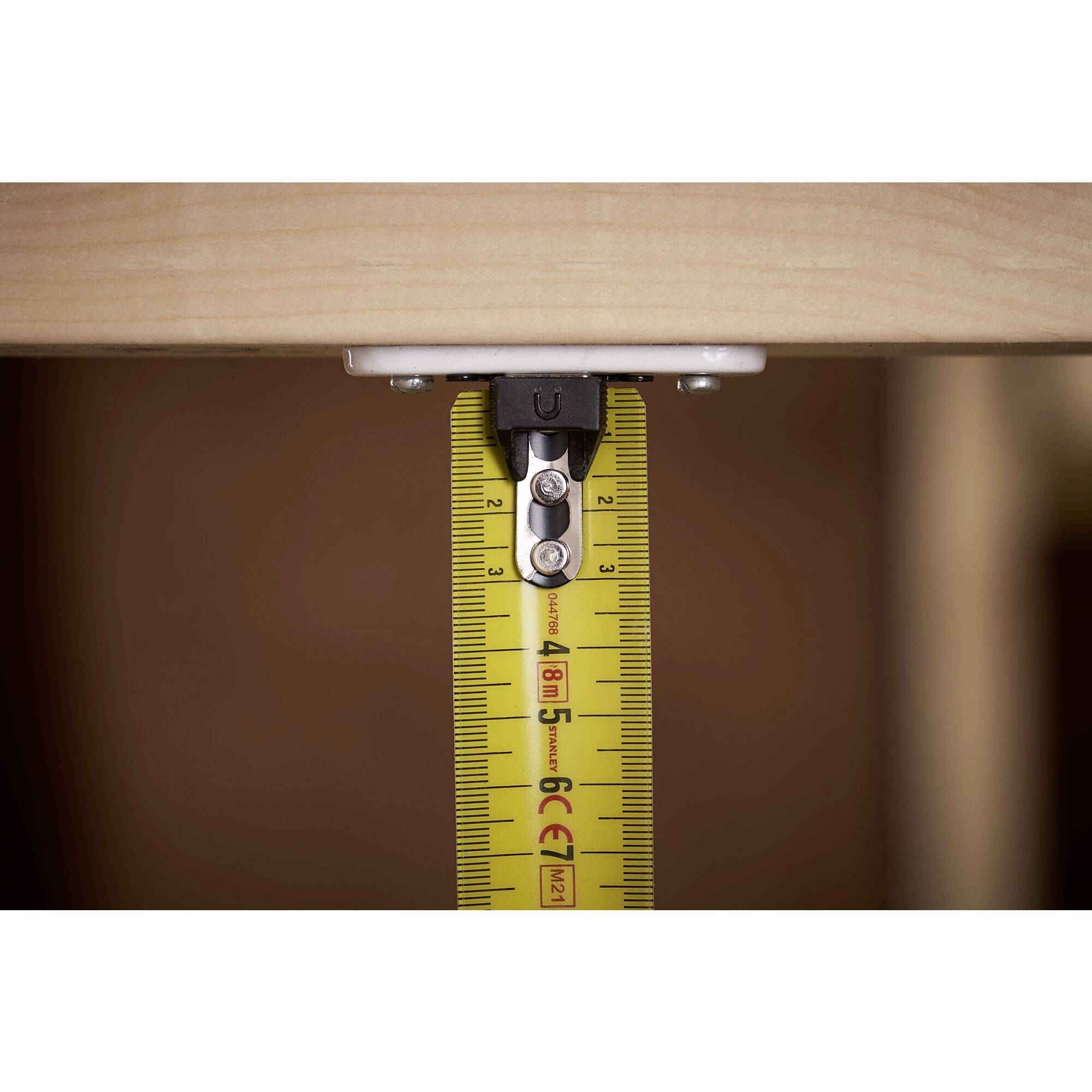 A tape measure is vertically fixed to a wooden edge and shows a straight measurement. It is held by a metal clip.
