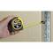 'A hand is holding an 8-metre Stanley FatMax tape measure, which is attached to a metal edge to measure a wall length.'