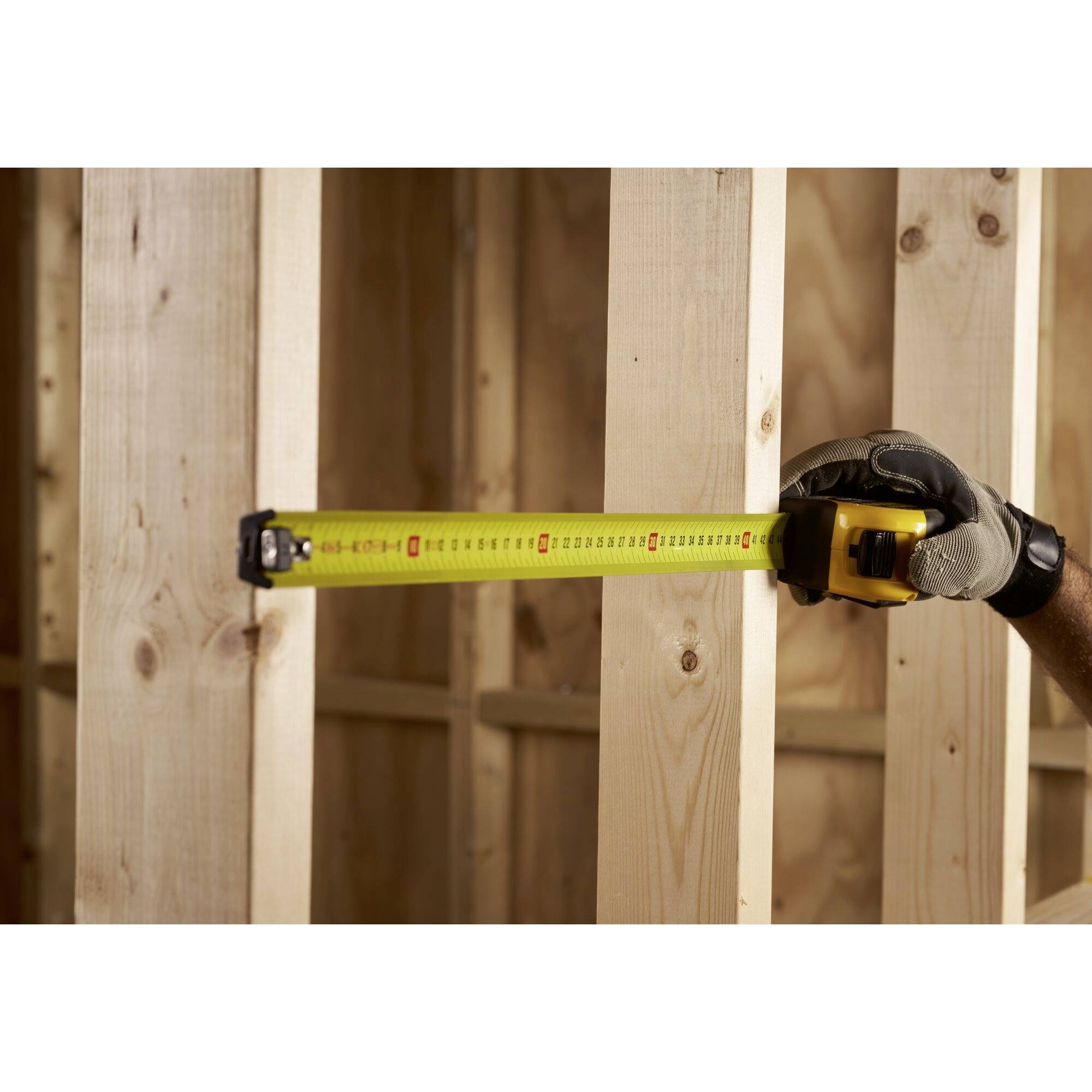 A worker is measuring the distance between two wooden beams with a yellow tape measure.