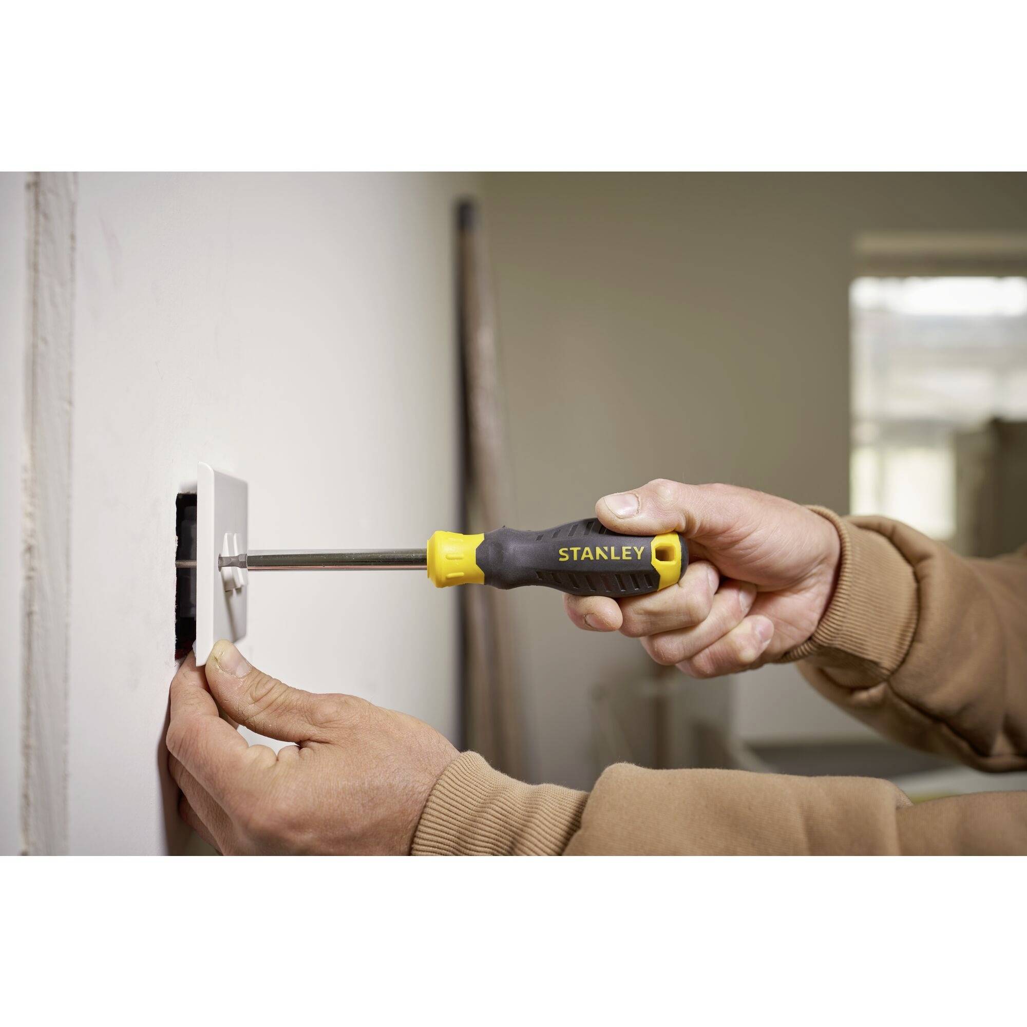 A person is repairing a plug socket on a wall using a screwdriver. The focus is on the handling of the tool.
