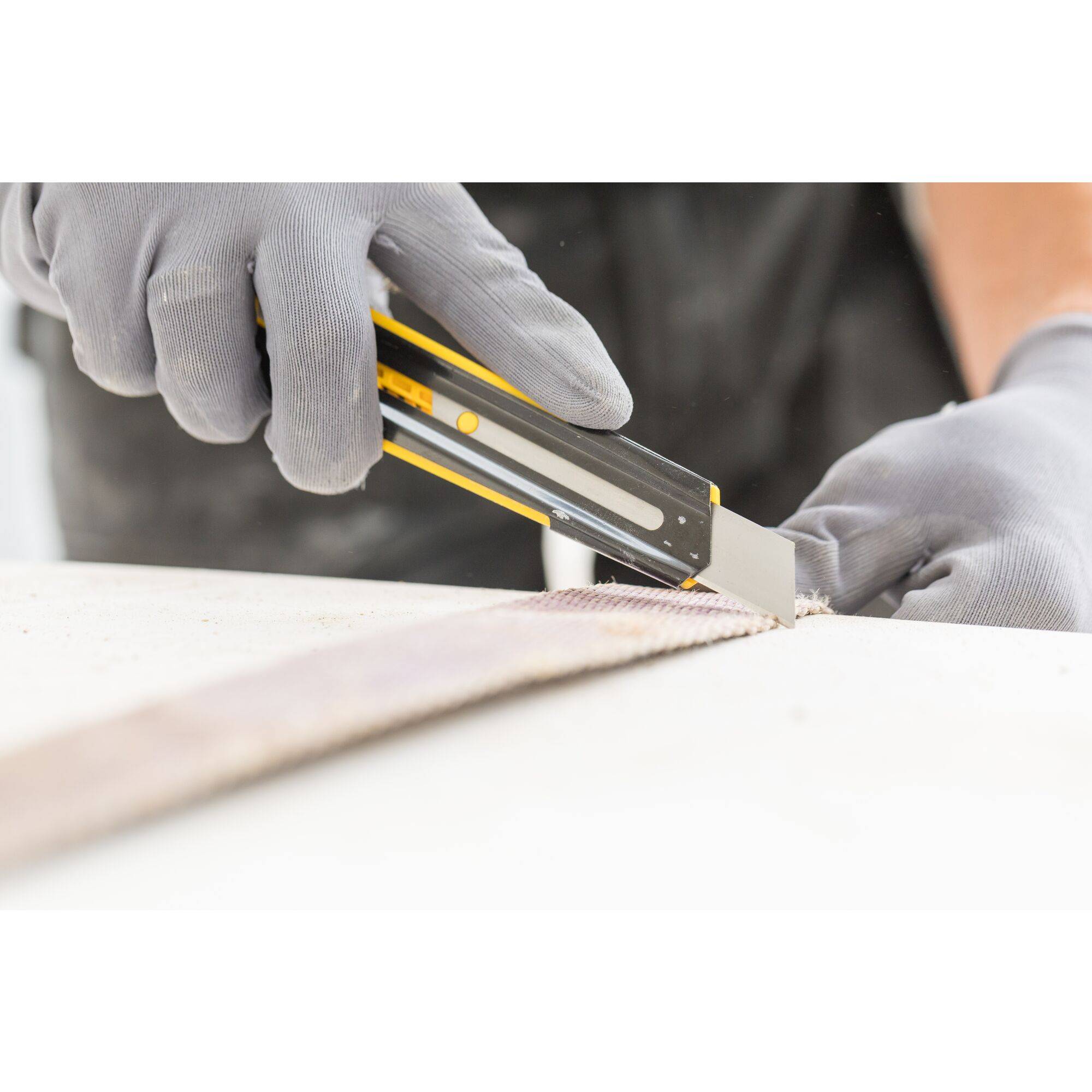A person is wearing grey gloves and cutting something with a craft knife on a flat surface.
