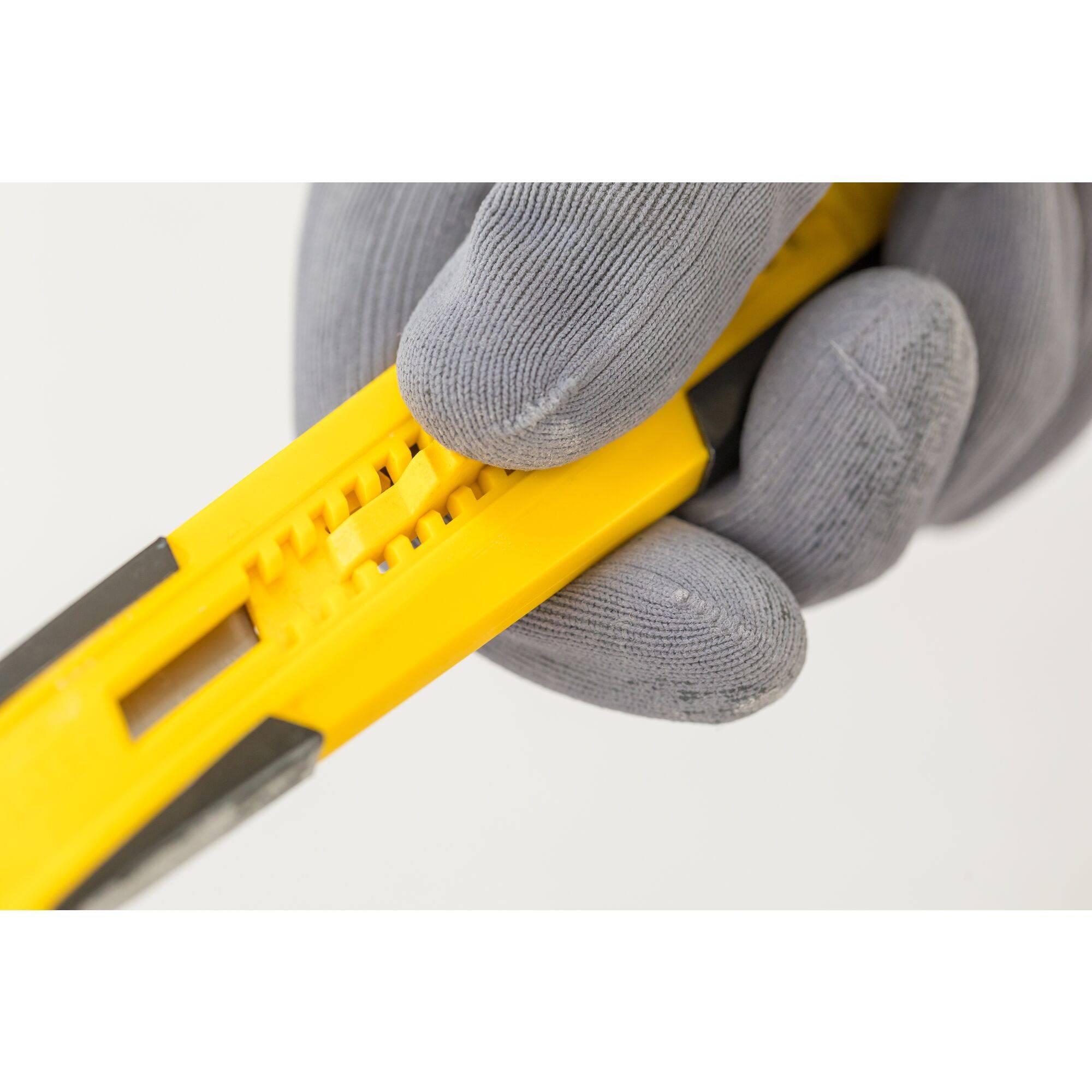 A gloved hand is holding a yellow carpet knife with an adjustable blade.