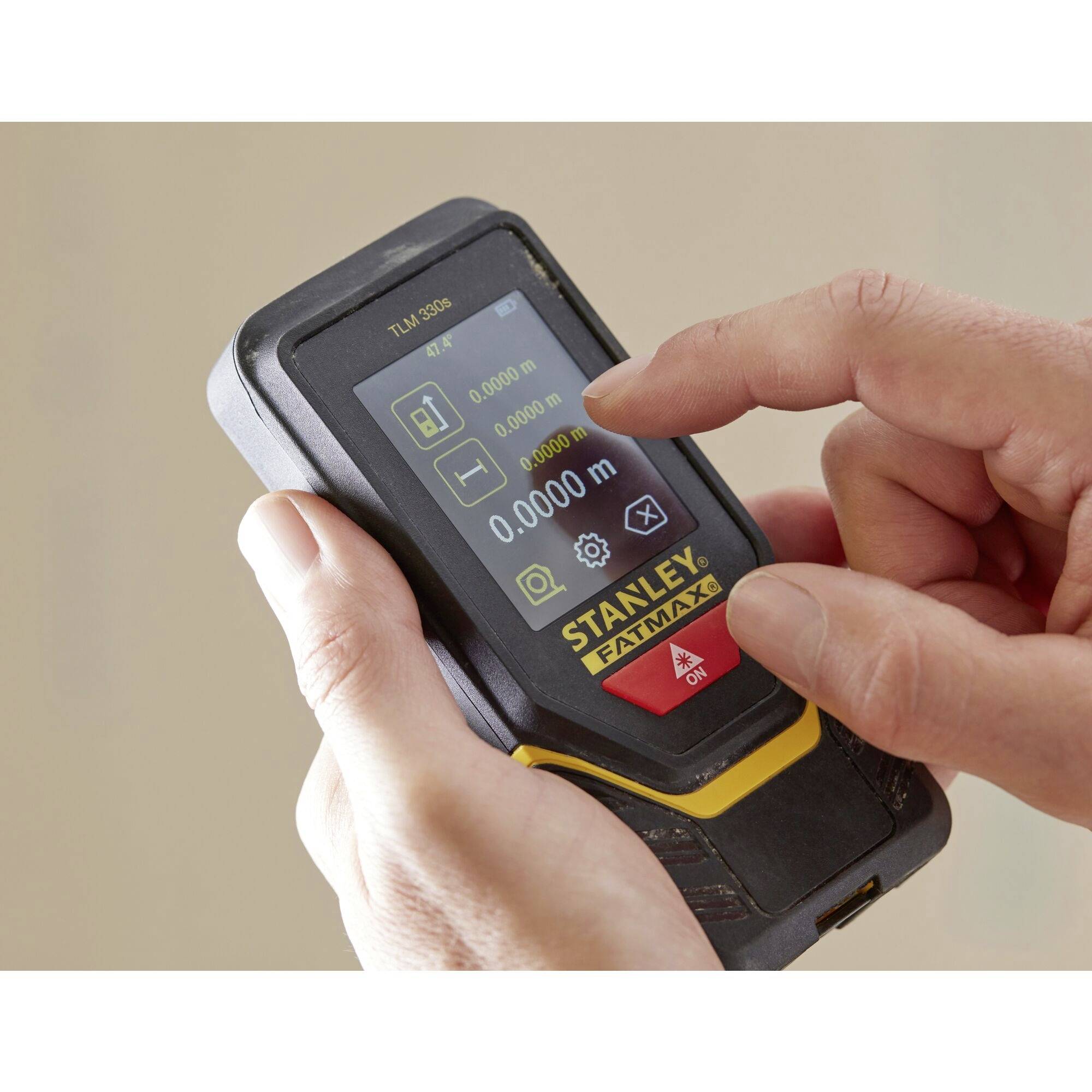 A person is holding a digital distance measurer with a display showing measurements in metres. The 'Stanley Fatmax' brand is visible.