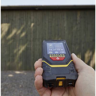 A hand holds a digital distance measuring device displaying '16.219 m' on its screen, while pointing at a wooden wall.