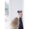 A person is measuring the distance on a white wall using a digital device, surrounded by a window frame with a view to the outside.