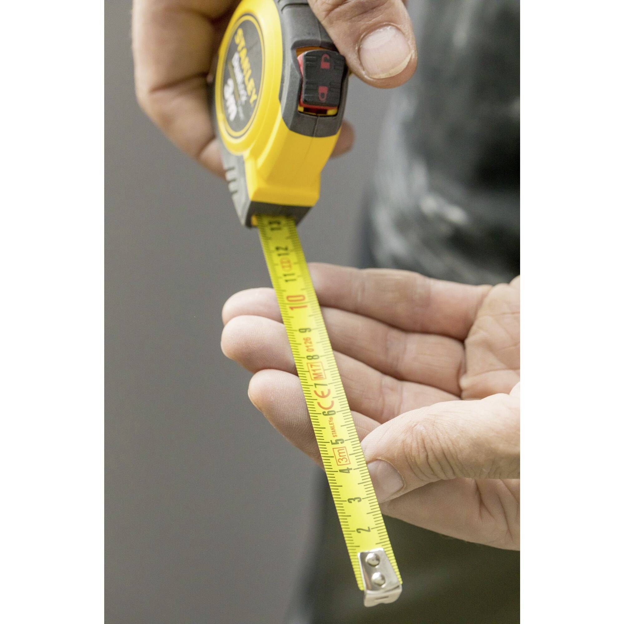 A person is holding a yellow tape measure between their hands while measuring a length.