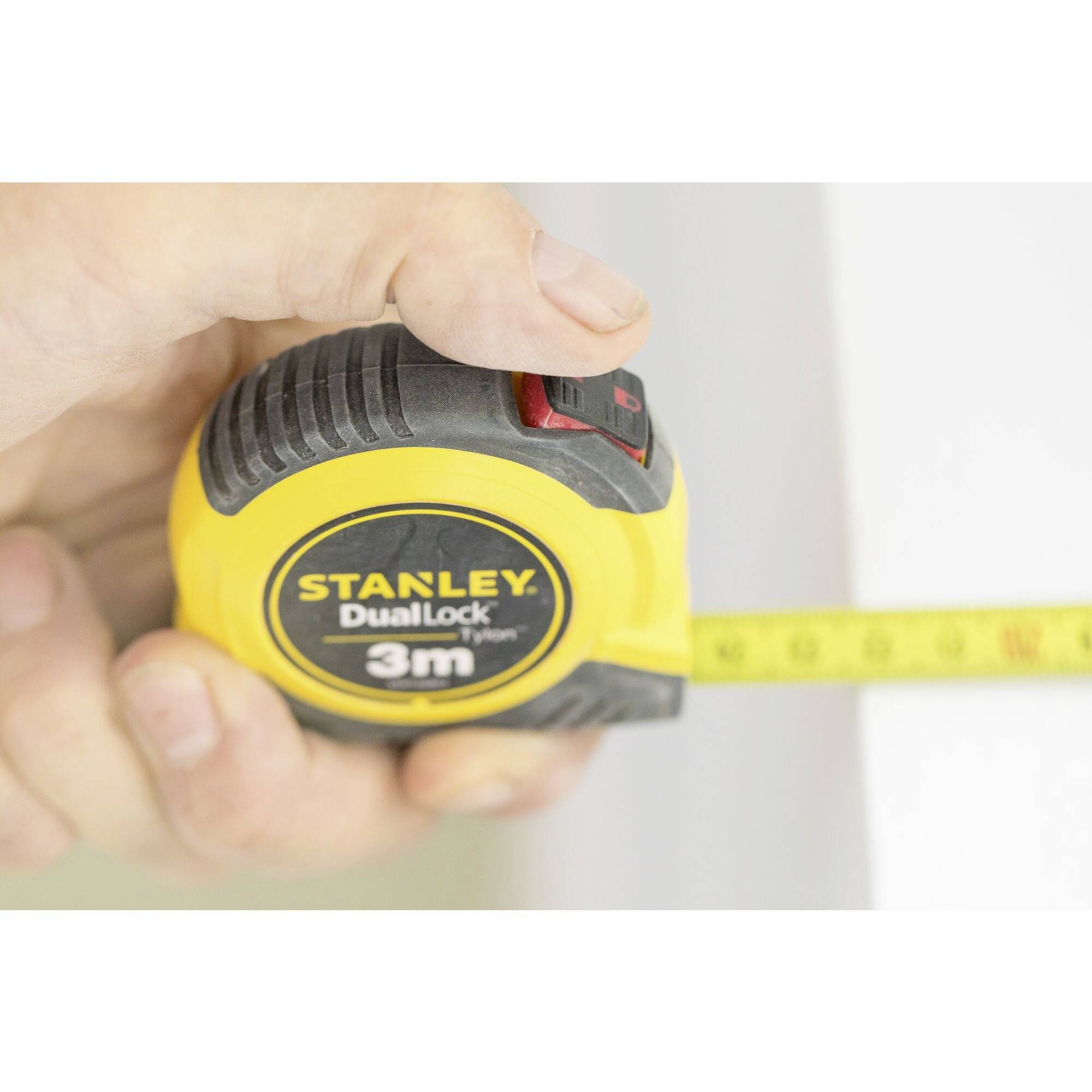 A hand is holding a yellow Stanley tape measure extended to 3 metres.