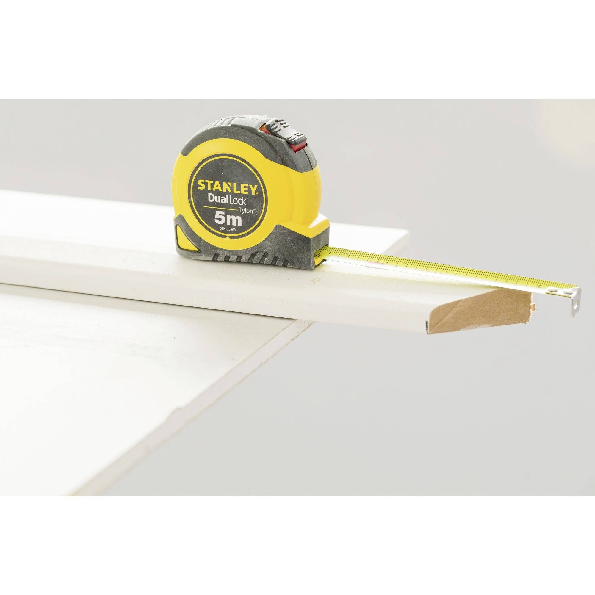 A yellow tape measure lies on a table, measuring a piece of wood that is broken off at the edge.