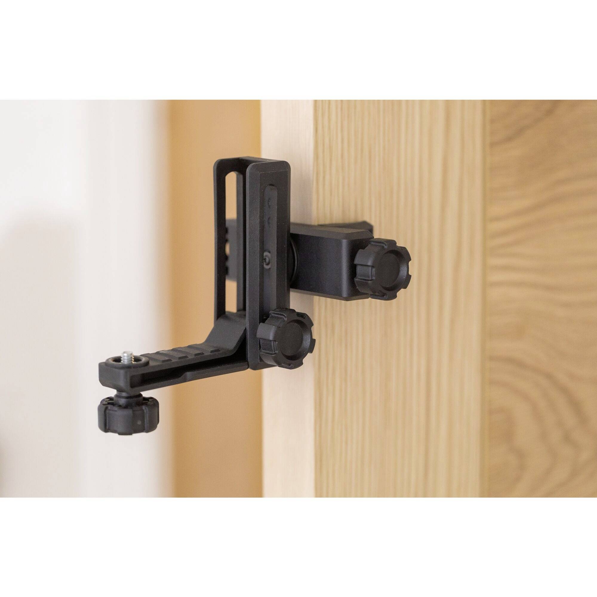 A black door stopper clip is attached at the top of an open wooden door, held in place by two adjustable screws.