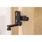A black door stopper clip is attached at the top of an open wooden door, held in place by two adjustable screws.