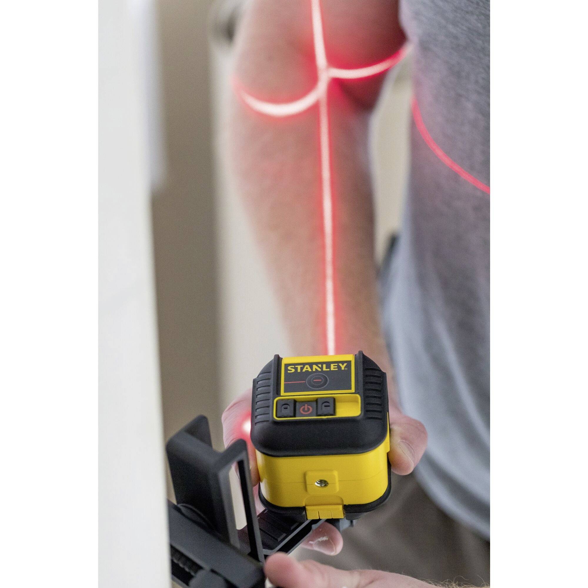 A person is using a laser levelling device on the wall. Red laser lines indicate vertical and horizontal levels.