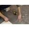 A person is aligning tiles on the floor using a laser distance measurer. Hands and tools are visible.
