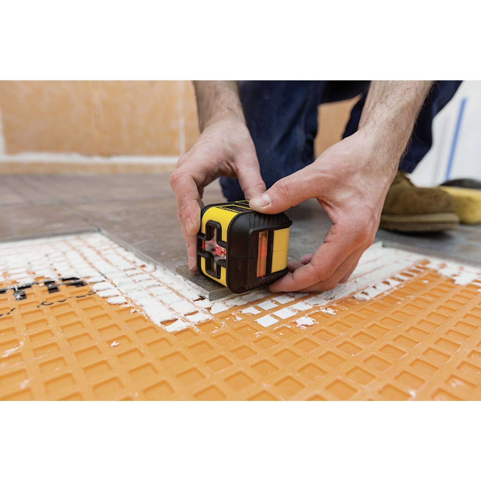 A person is positioning a yellow spirit level on an orange floor mat. Hands and tool are the focal point.