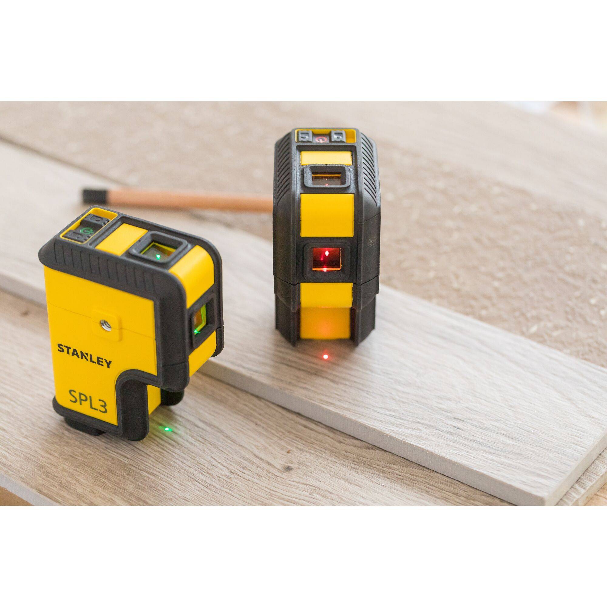 Two yellow laser levelling devices on a wooden surface; one showing a green laser, the other sweeping a red laser; construction tool setting.