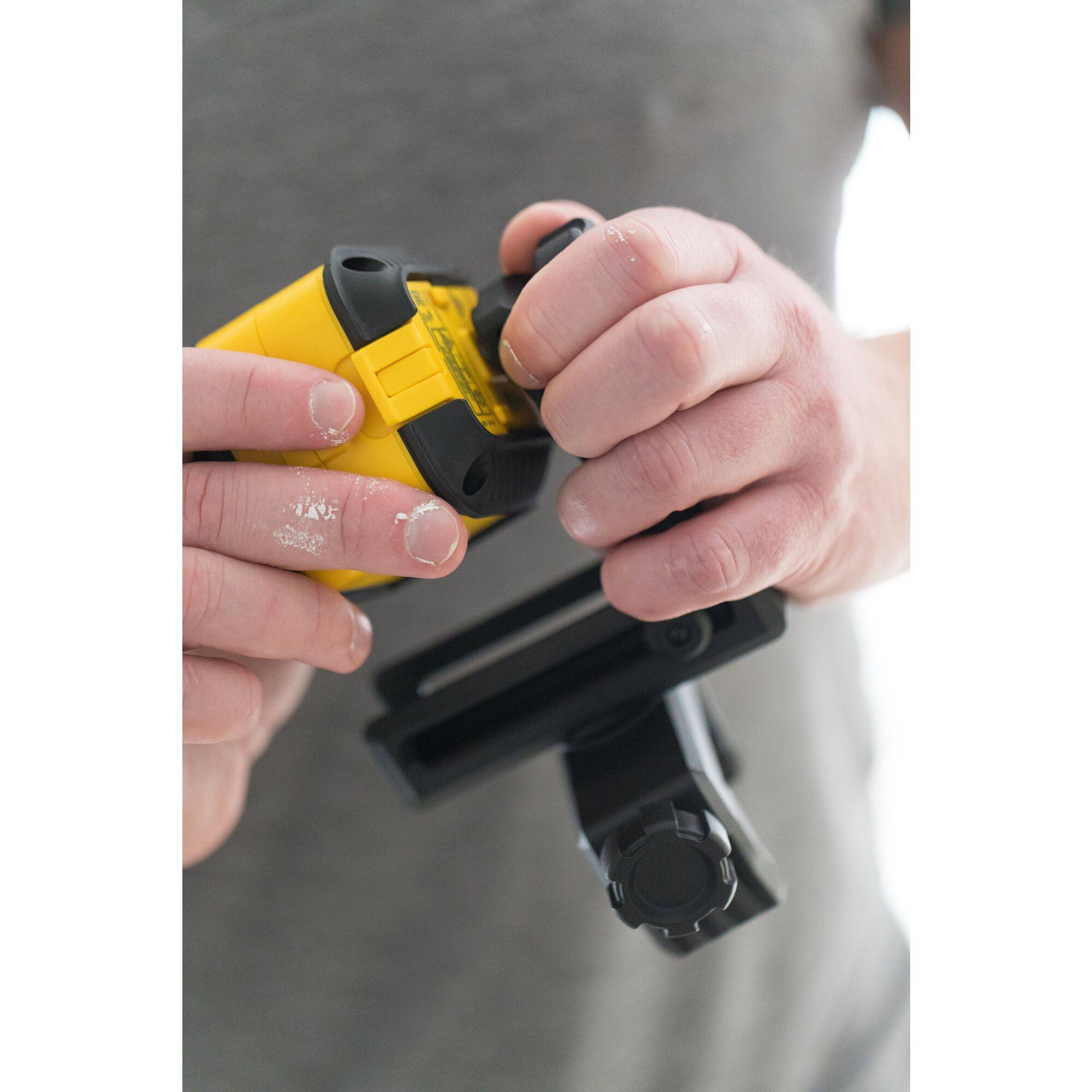 A person is holding a yellow tool with a black handle. A black tripod or mount is also visible.