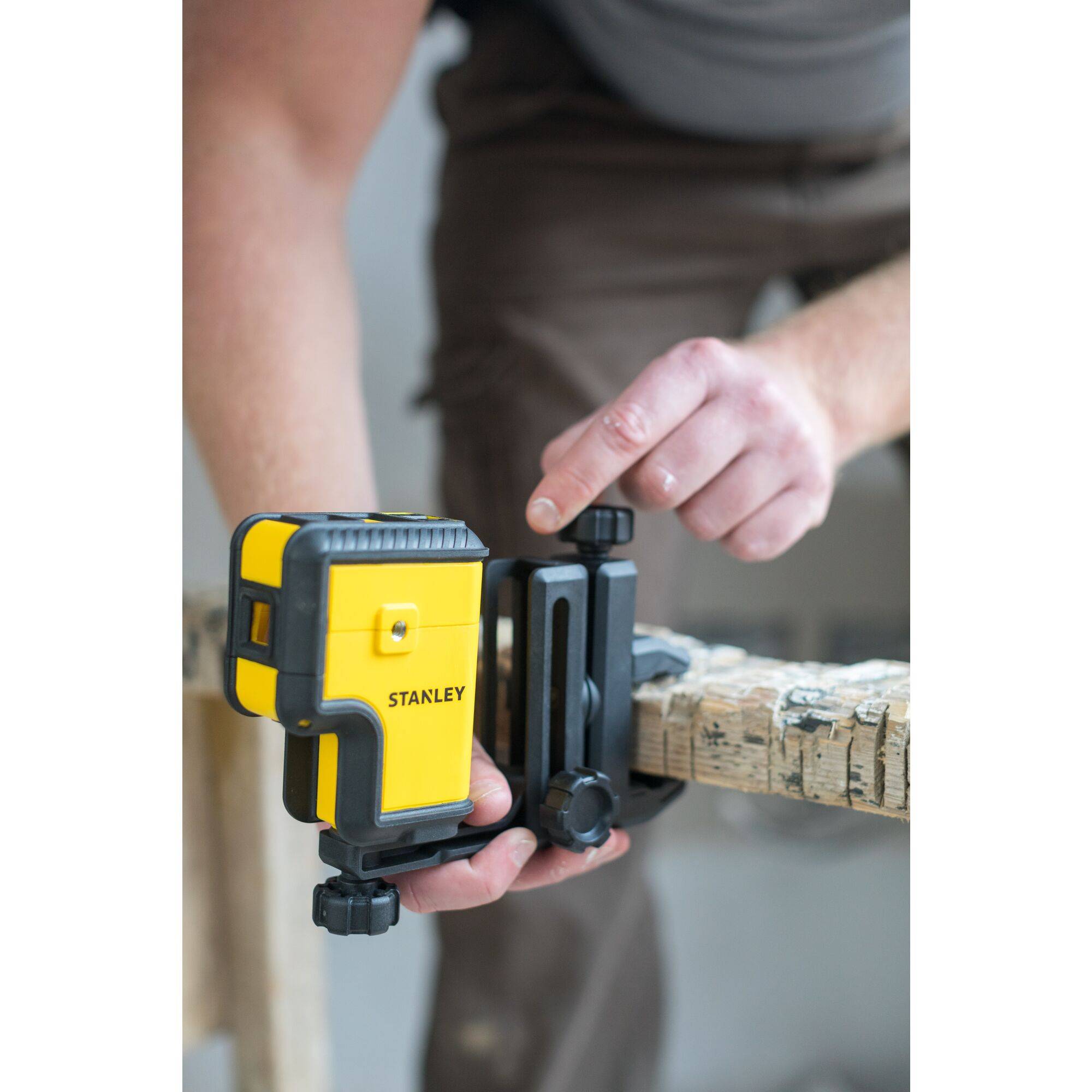 A yellow laser instrument by the brand 'STANLEY' is being secured by a person on a structured surface.