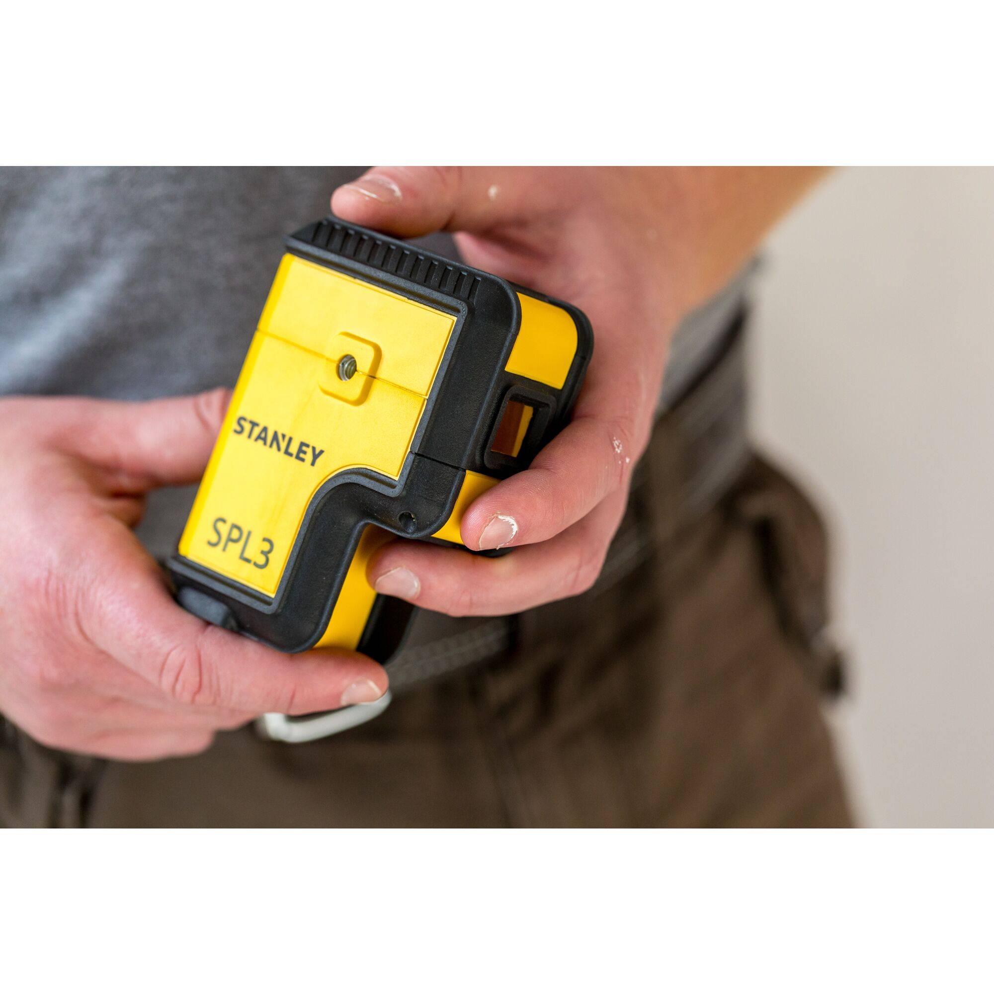 A person is holding a yellow laser distance measuring device in their hand. The device has the 'Stanley SPL3' logo printed on it.