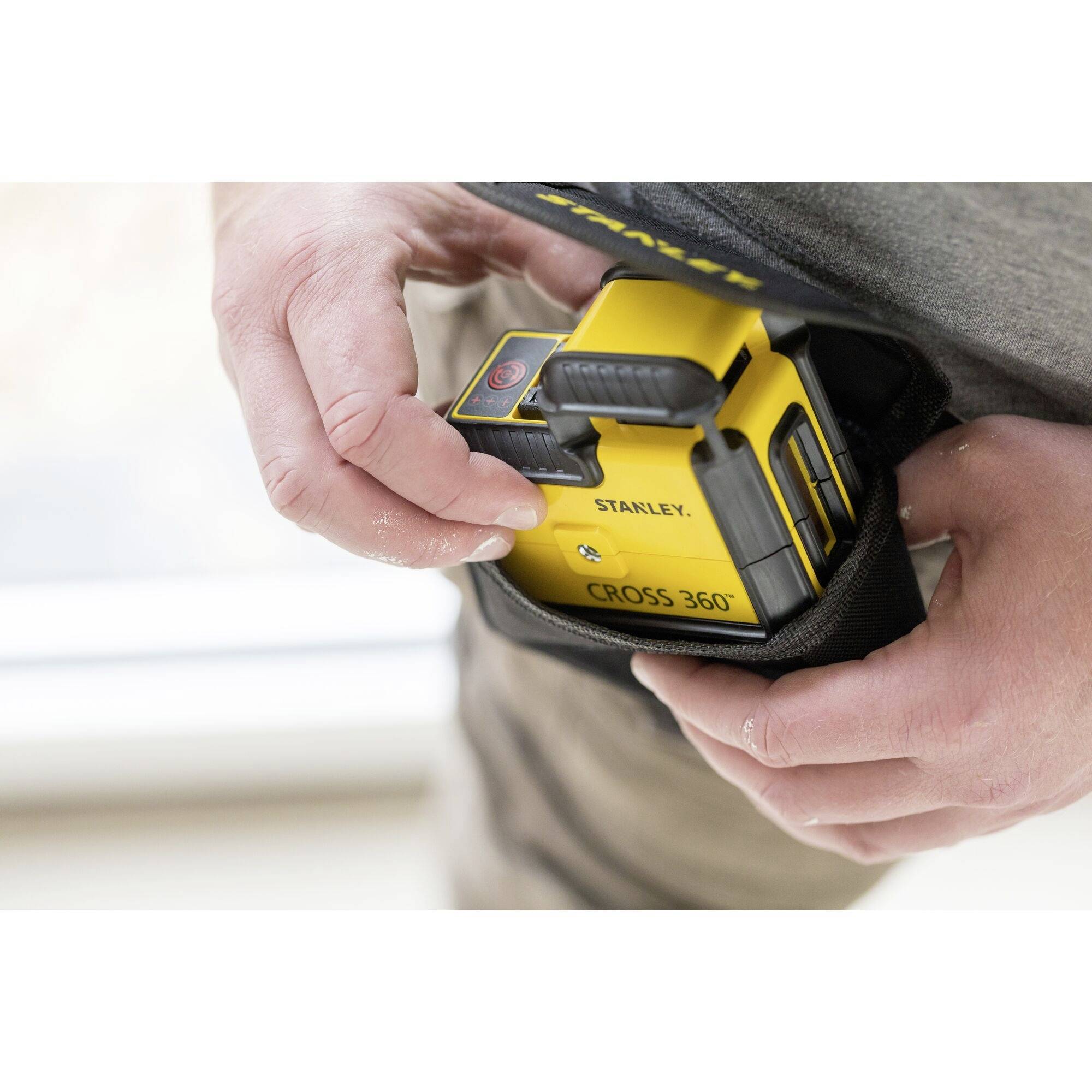 A person is holding a yellow laser measuring device in their hands, ready for use. The device is from the Stanley brand.