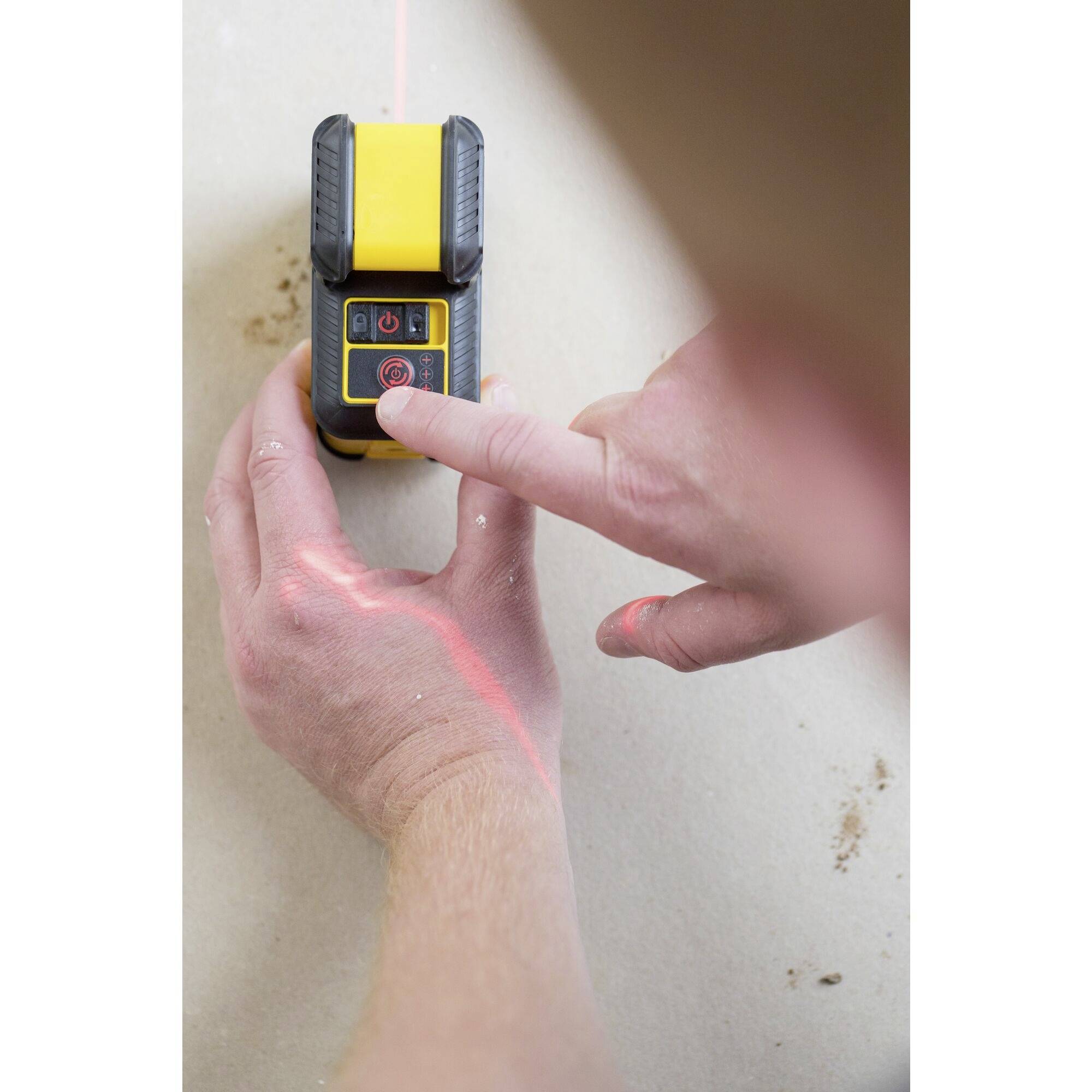 A person is using a yellow laser measuring device to align a straight line on a surface. The laser beam is red.