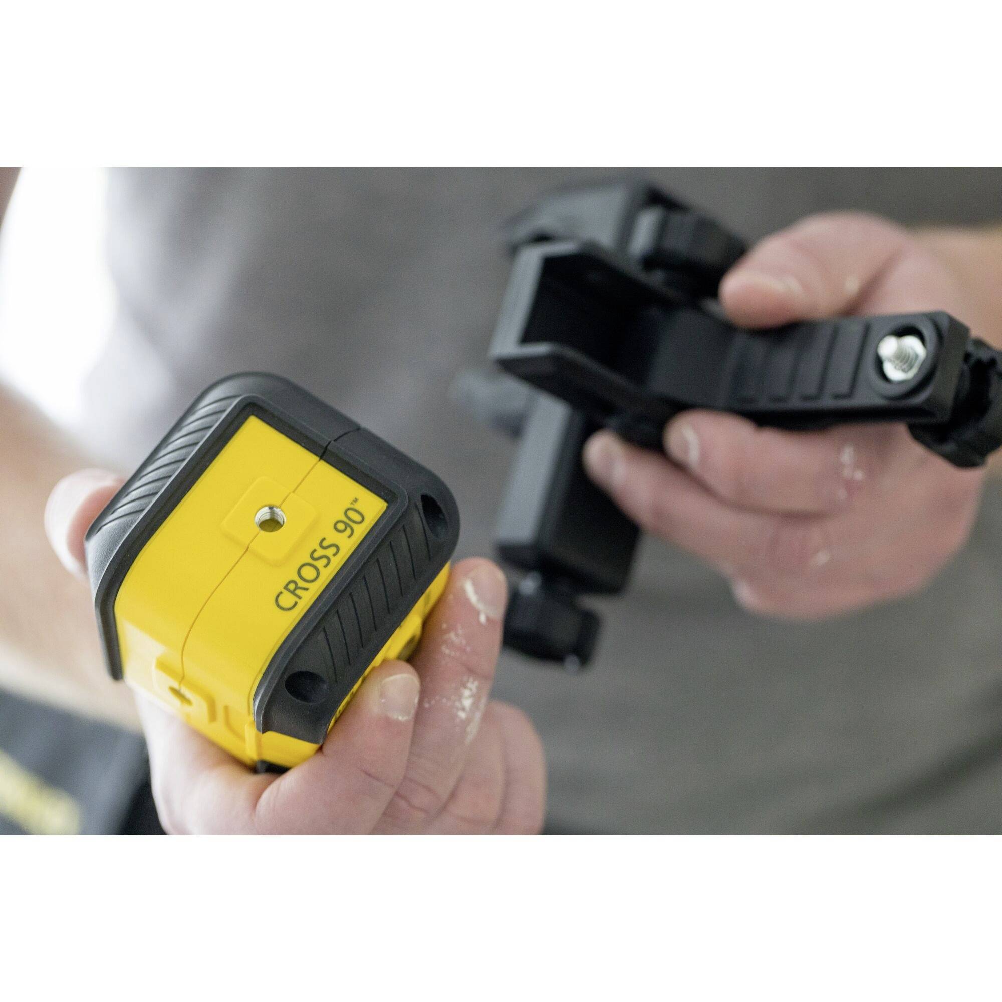 A person is holding a yellow measuring tool with the inscription 'CROSS 90°', attached to a black mount. Focus is on the device.