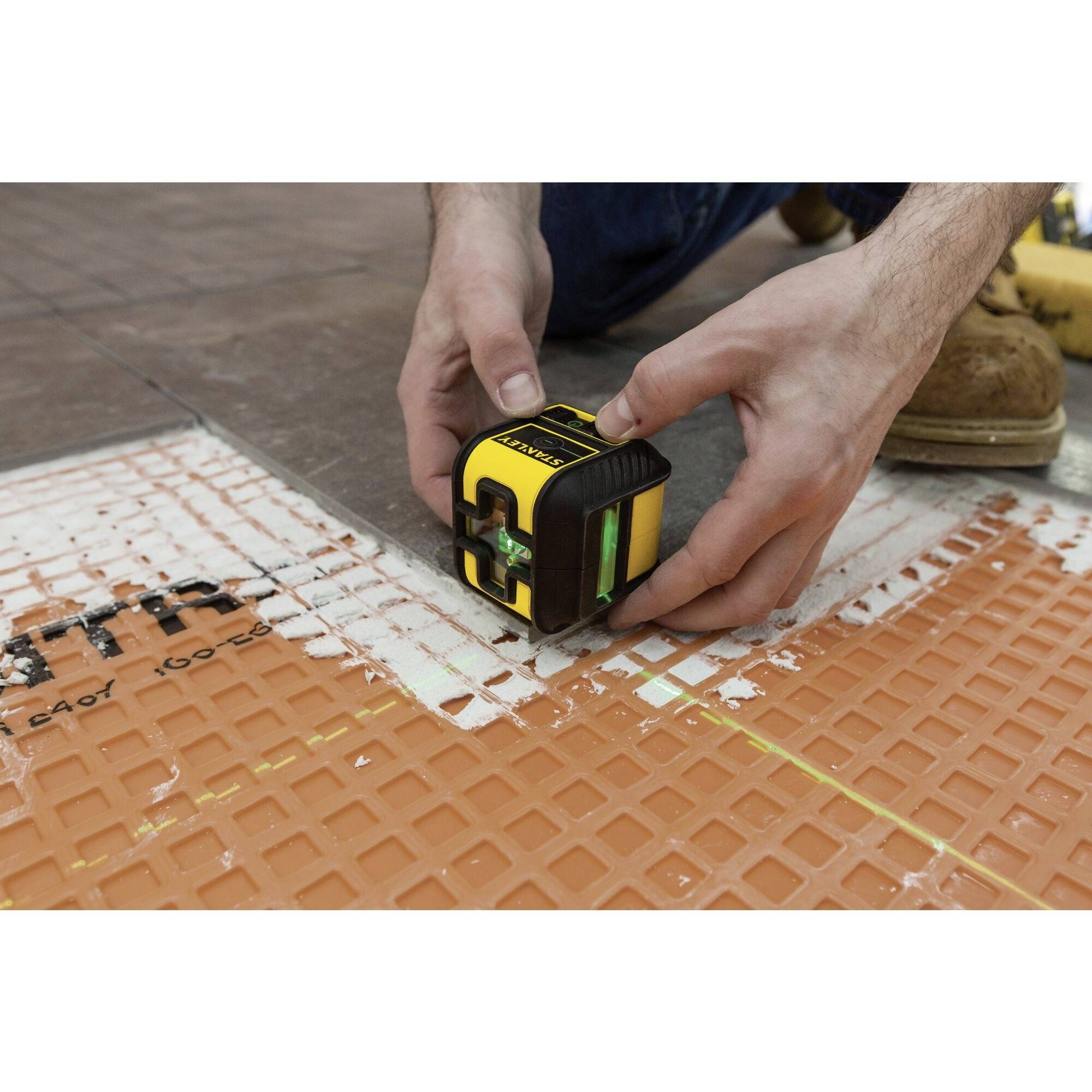 A person is using a laser tool to measure and align floor tiles with precision.