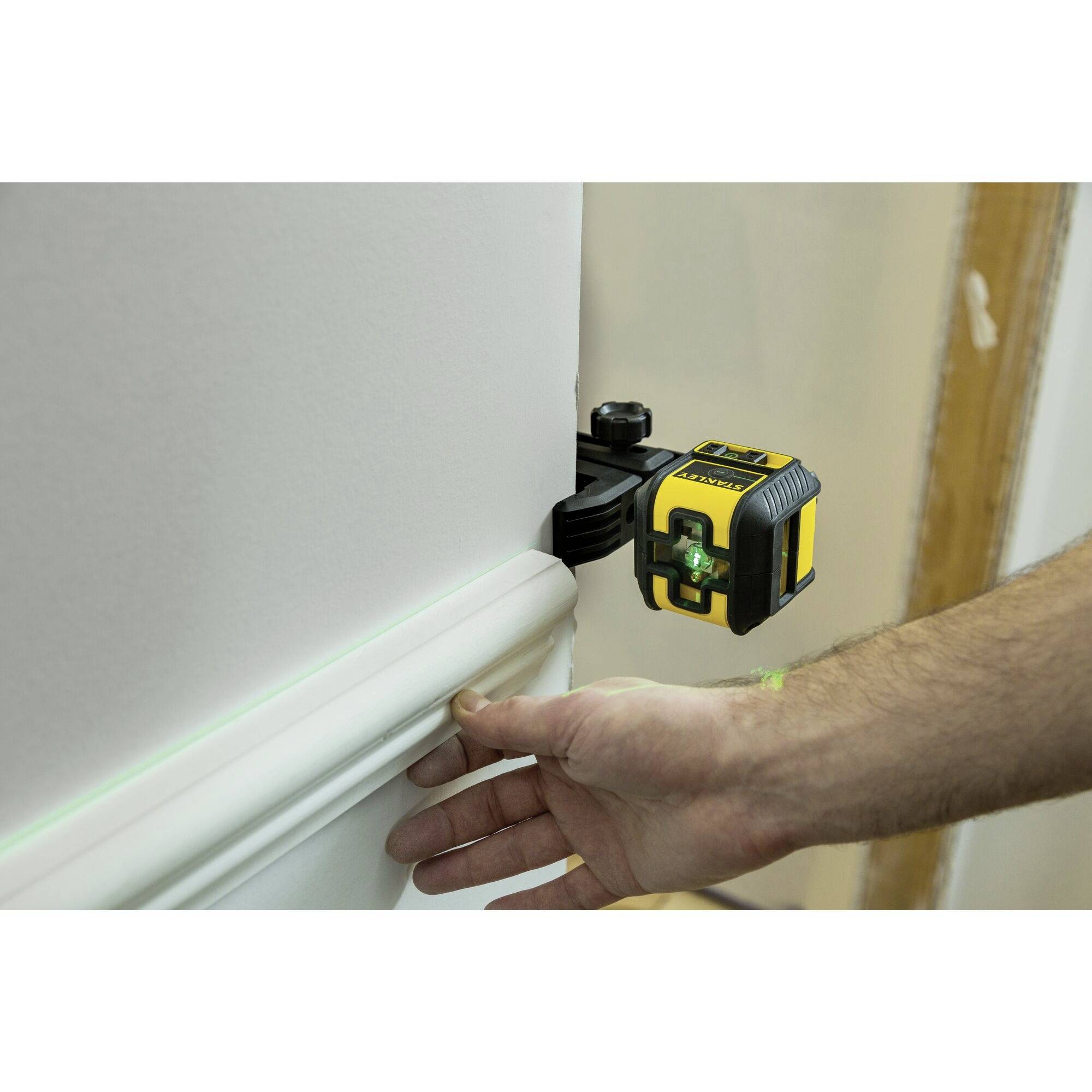 A person is aligning a spirit level on a wall using a digital laser tool. The device is projecting green lines.