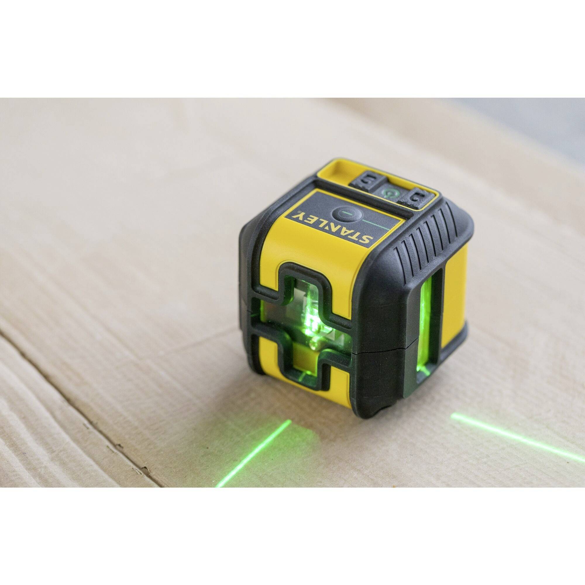 A yellow and black laser measuring device is projecting green lines onto a wooden surface for precise measurement.