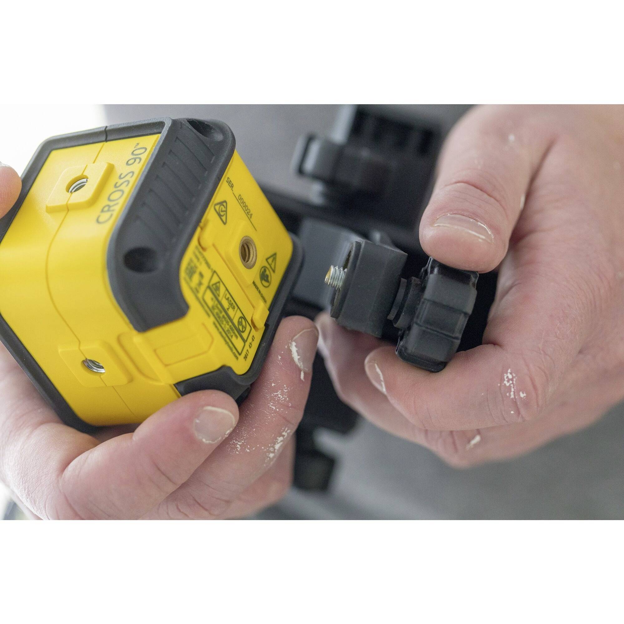 A person is holding a yellow laser level in their hands. The device is being adjusted or prepared for use.