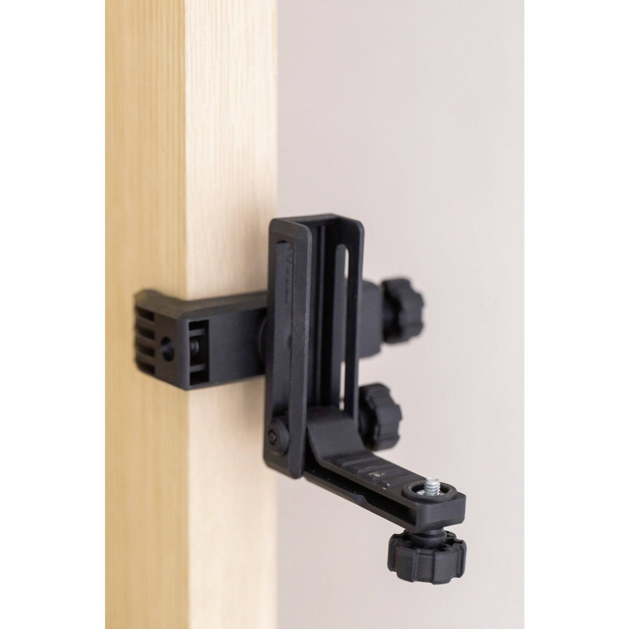 A black door anchor for fitness bands is attached to a wooden frame. It has multiple adjustment knobs for optimal positioning.
