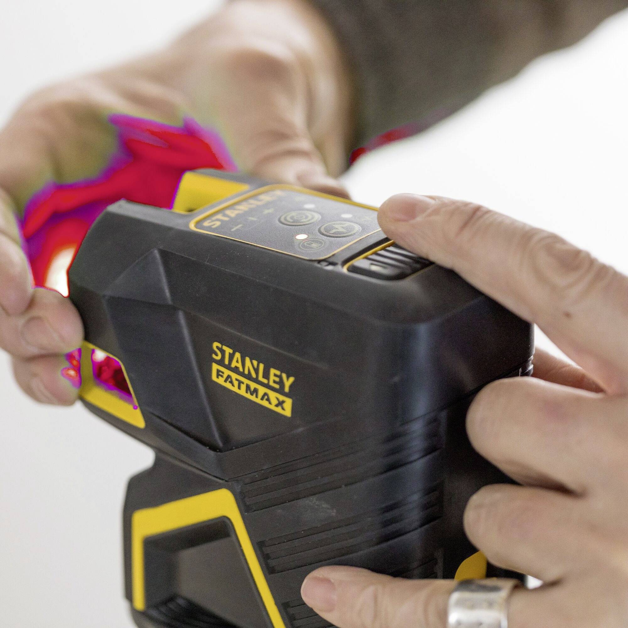 A person is holding a black Stanley Fatmax laser tool with a yellow logo. They are adjusting it to use it.